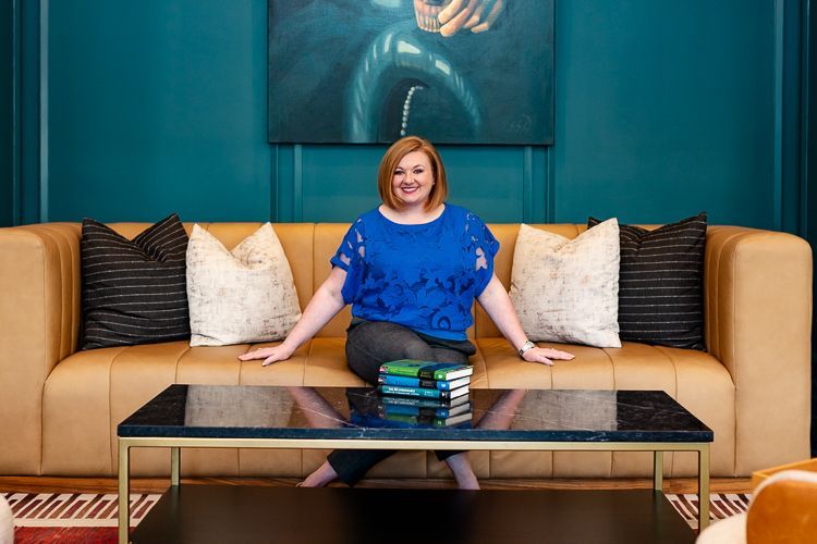 A woman in a green shirt is sitting on a couch with her hand on her chin.