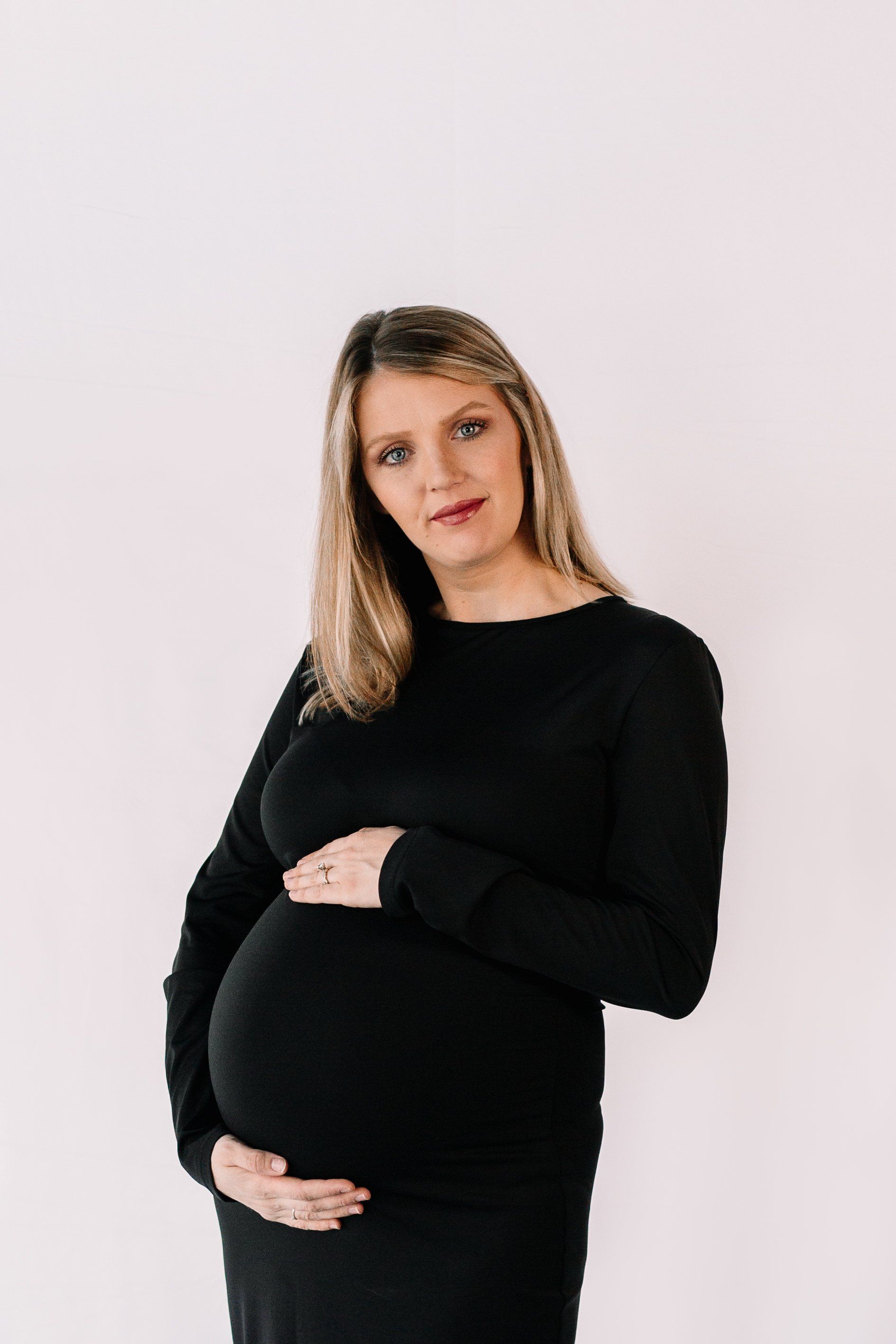 A pregnant woman in a black dress is holding her belly.