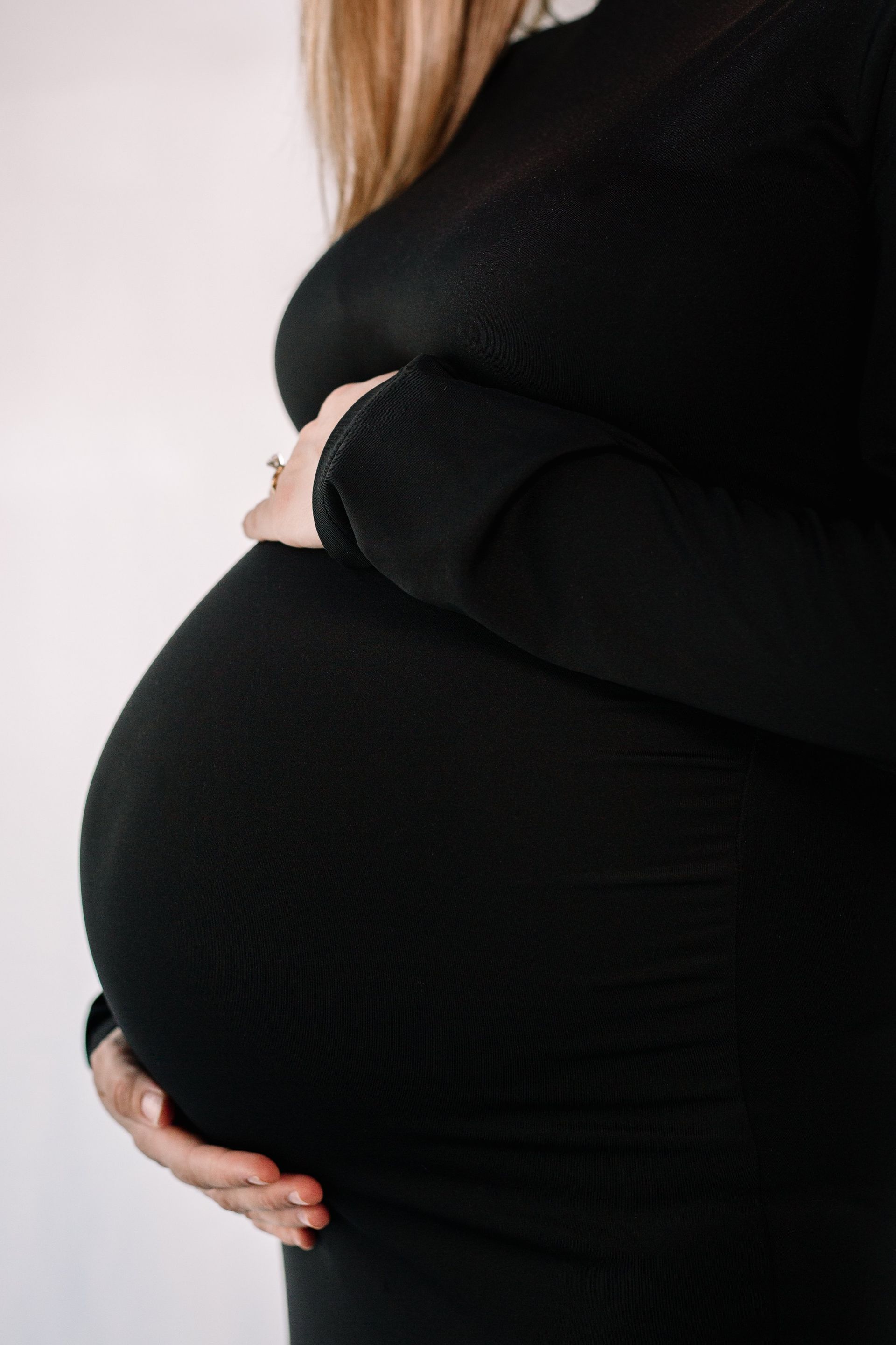 A pregnant woman in a black dress is holding her belly.