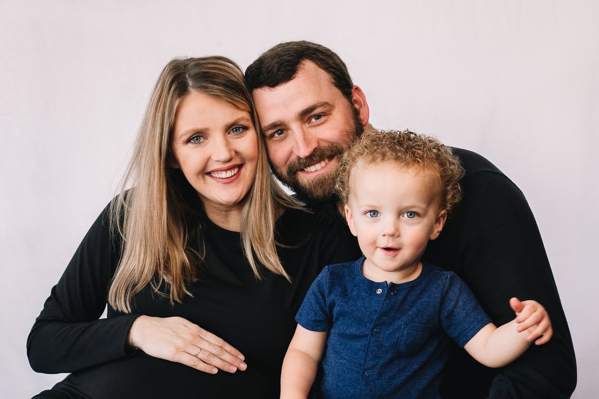 A pregnant woman , a man and a child are posing for a picture.