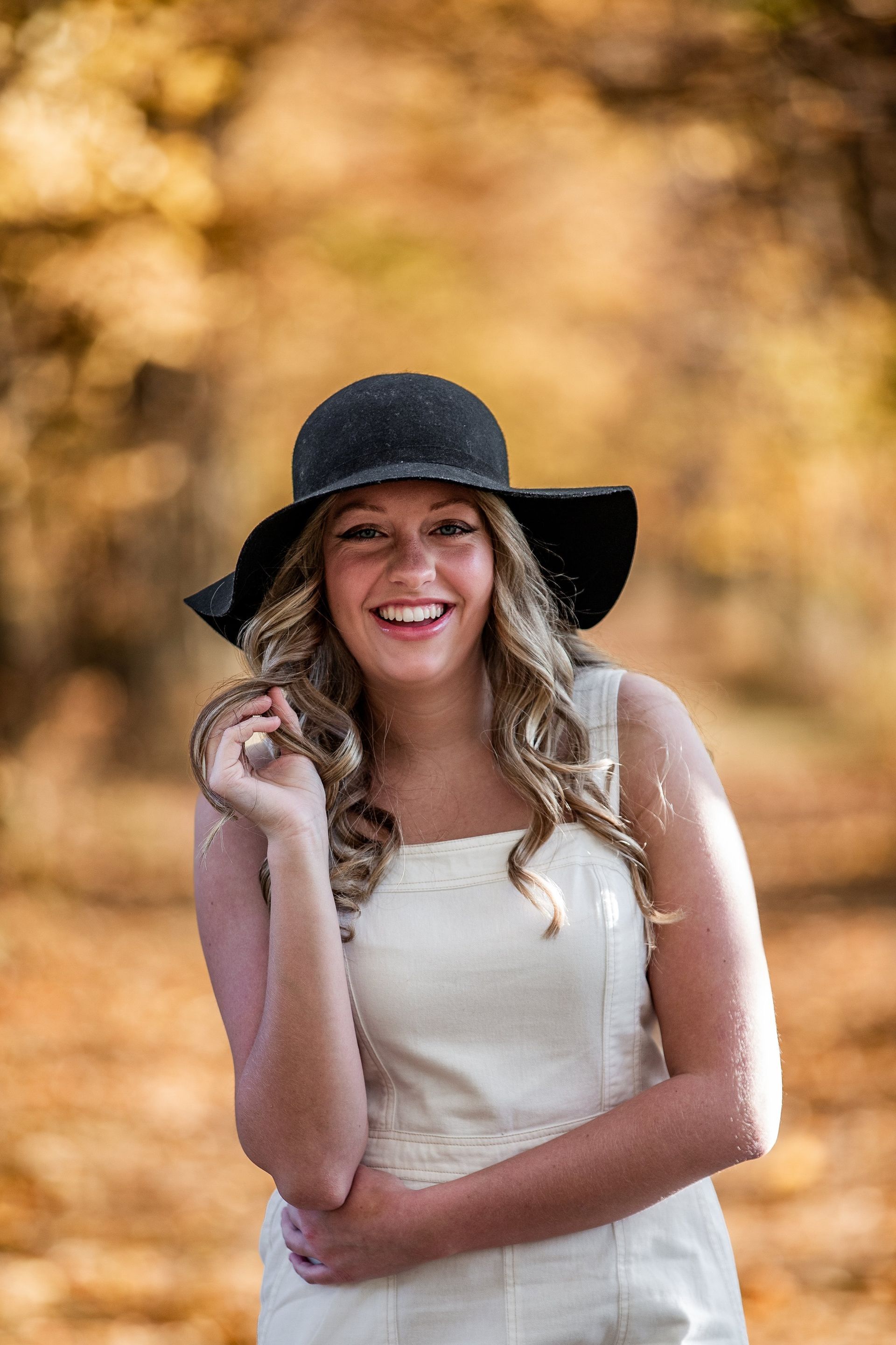 A woman wearing a hat and a white dress is smiling.