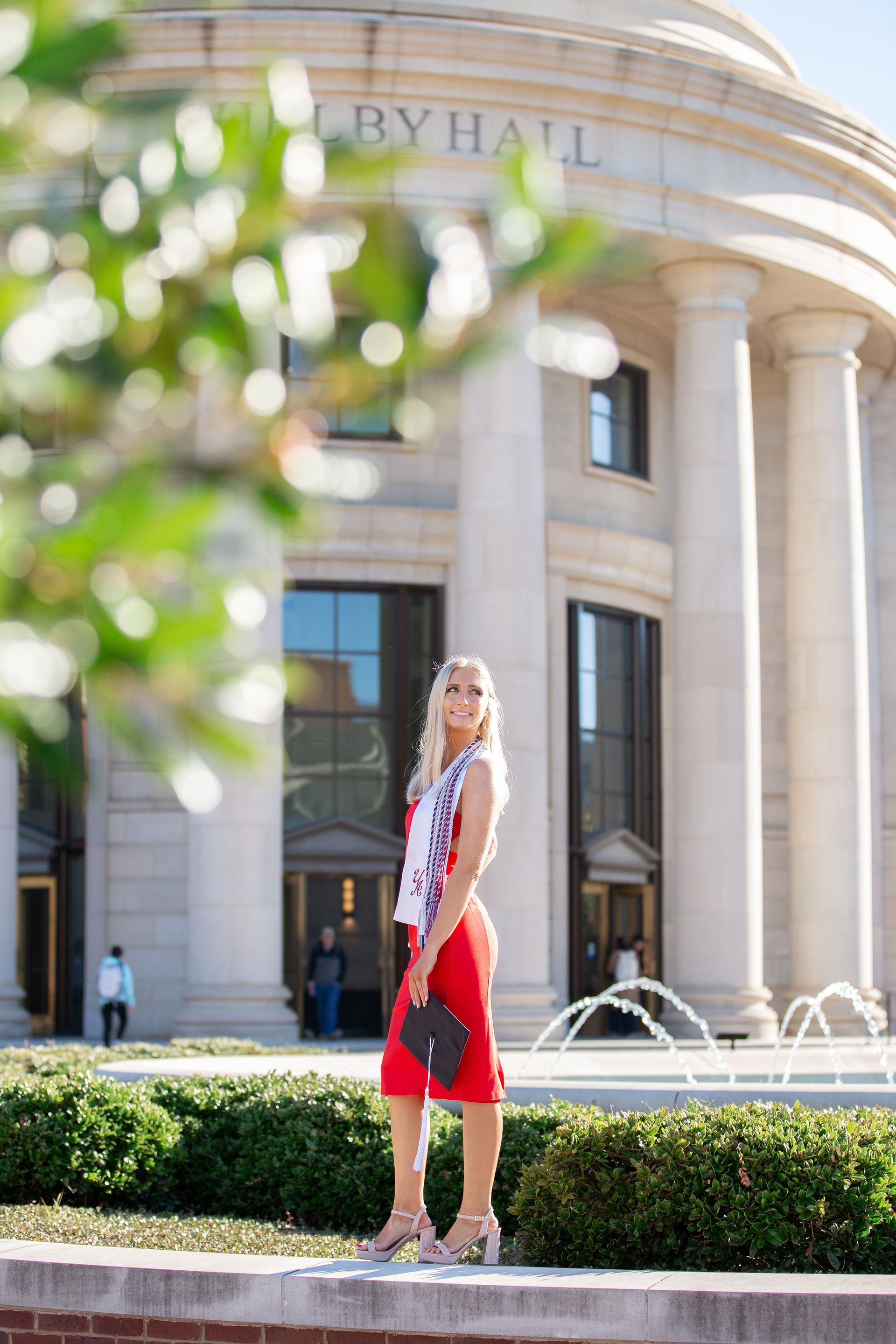 A woman in a red dress is standing in front of a building.