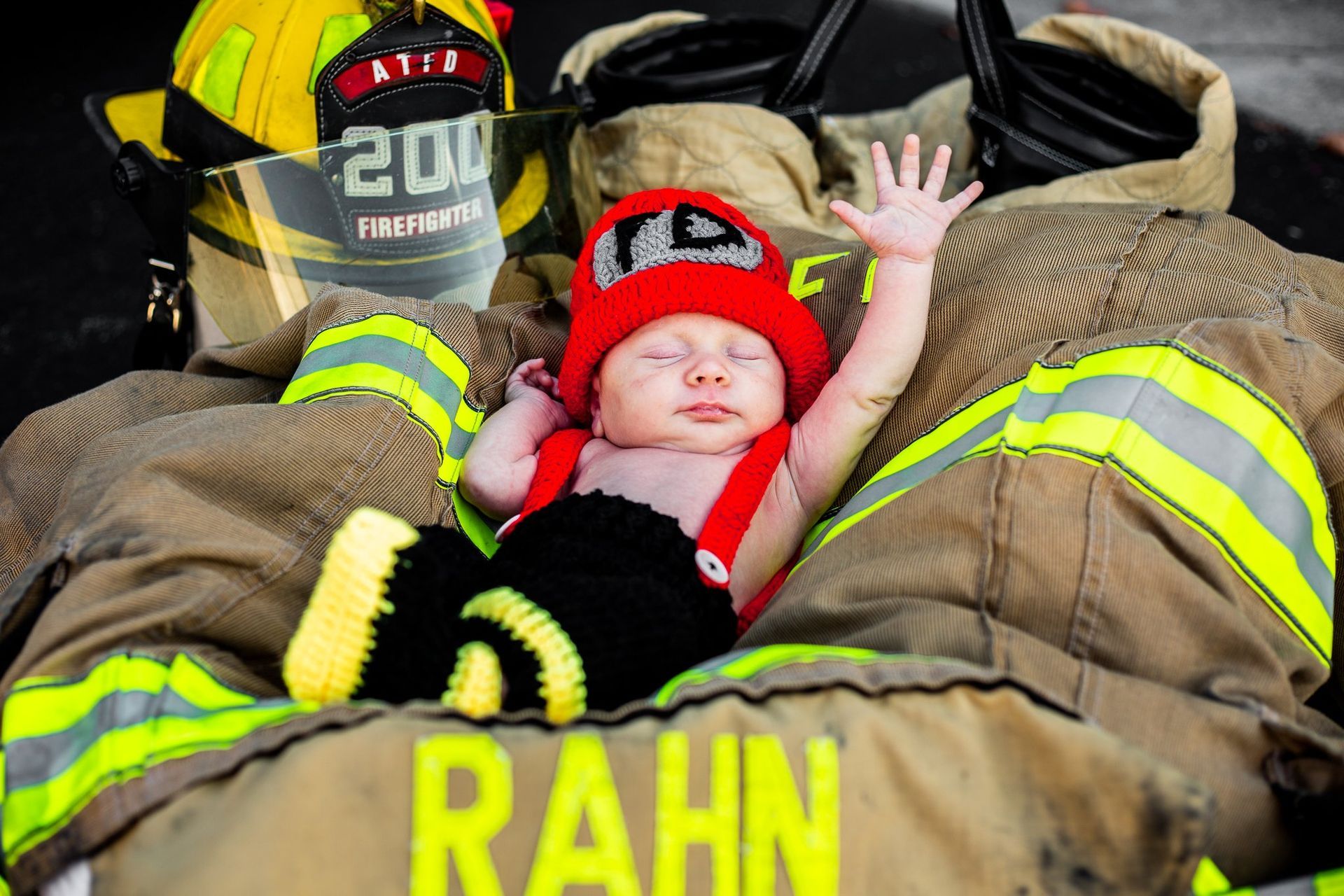 A baby dressed as a fireman is laying on a fireman 's jacket.