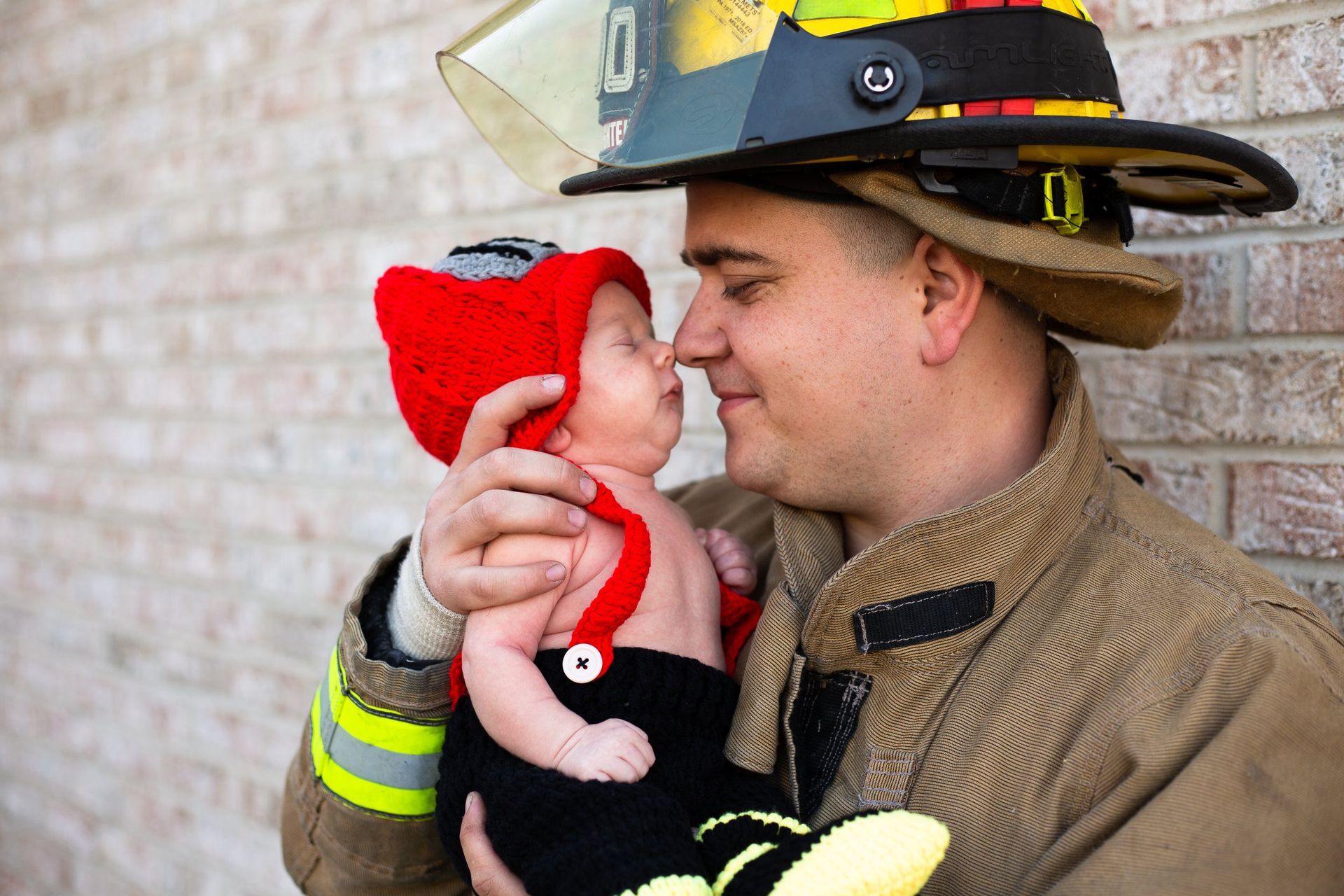 A fireman is holding a baby in his arms and the baby is wearing a red hat.