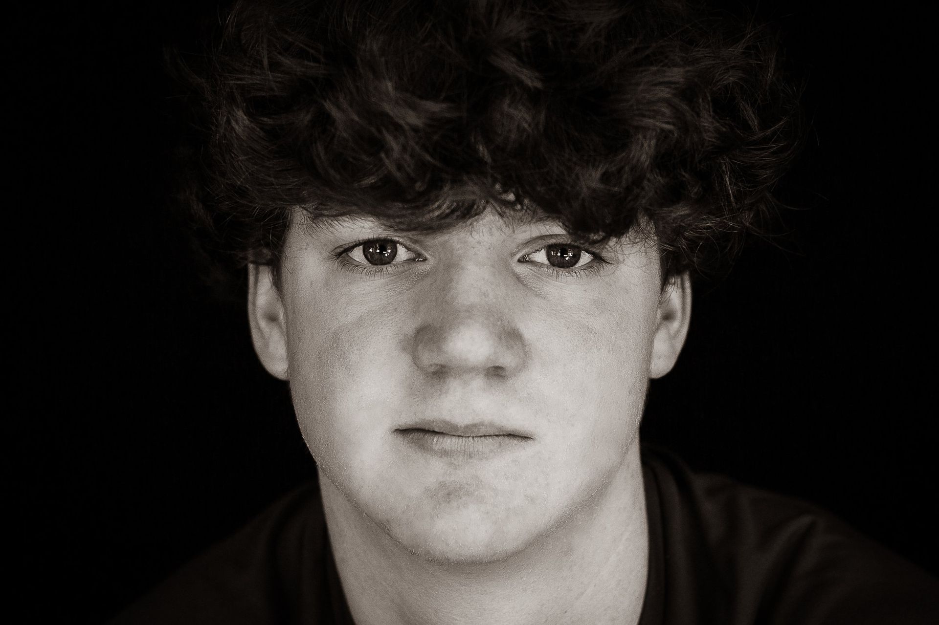 A young man with curly hair is looking at the camera in a black and white photo.