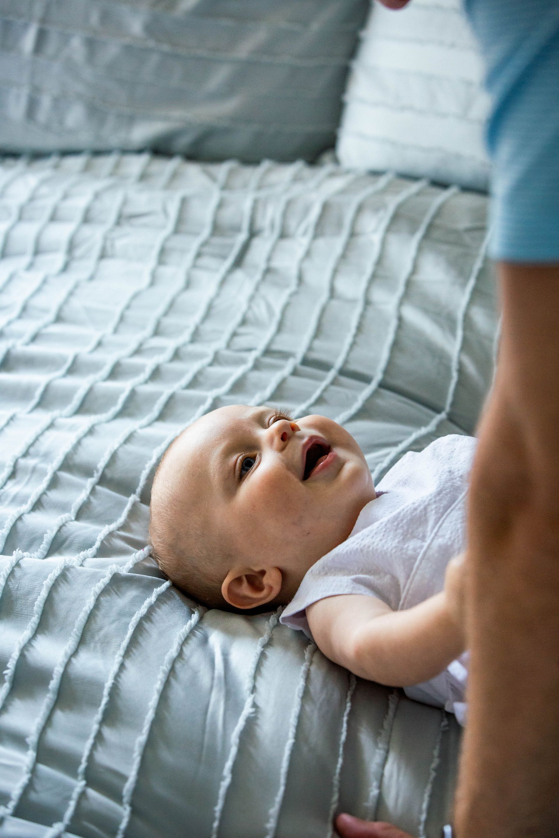 A baby is laying on a bed with a person standing next to it.