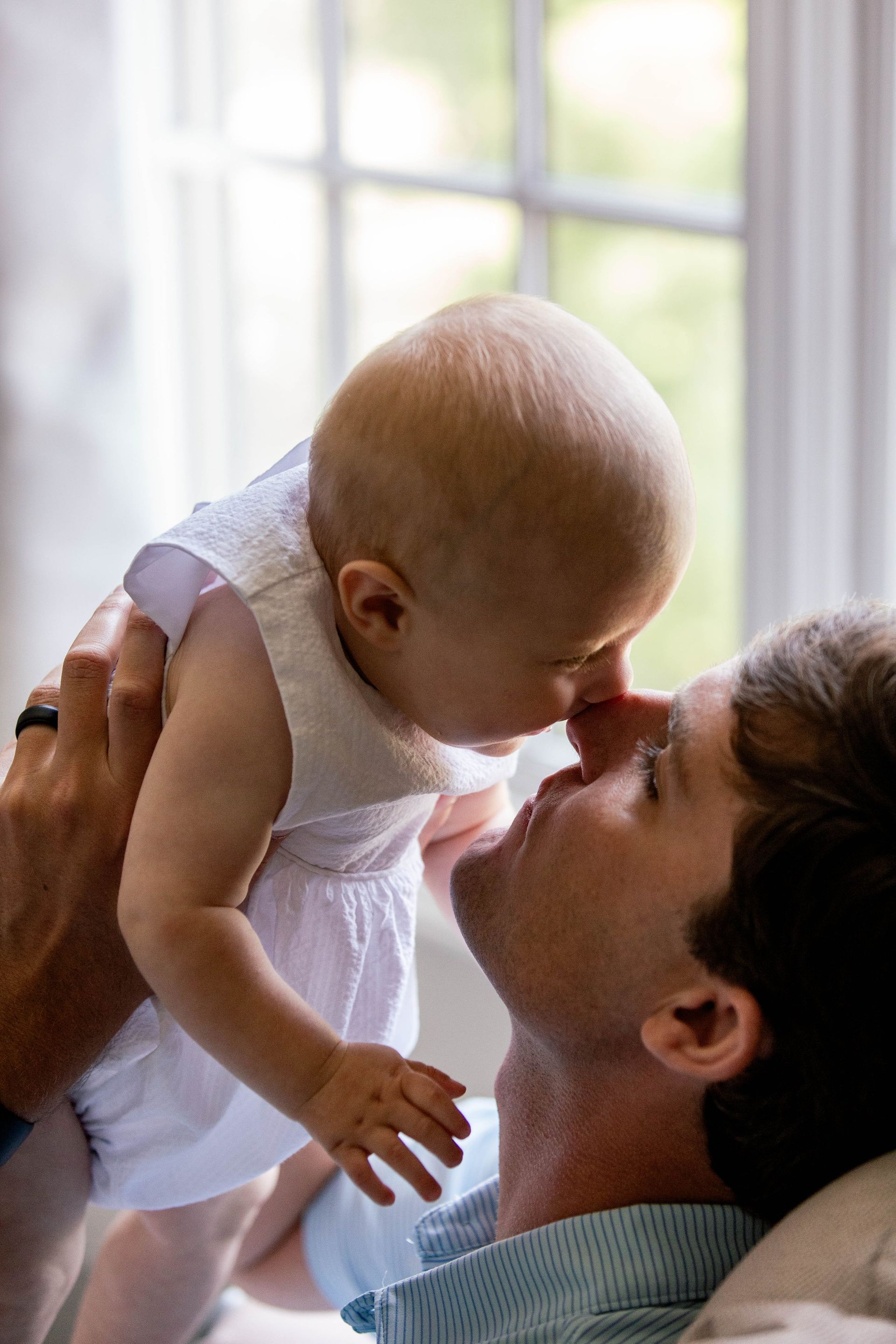 A man is holding a baby in his arms and the baby is touching the man 's nose.