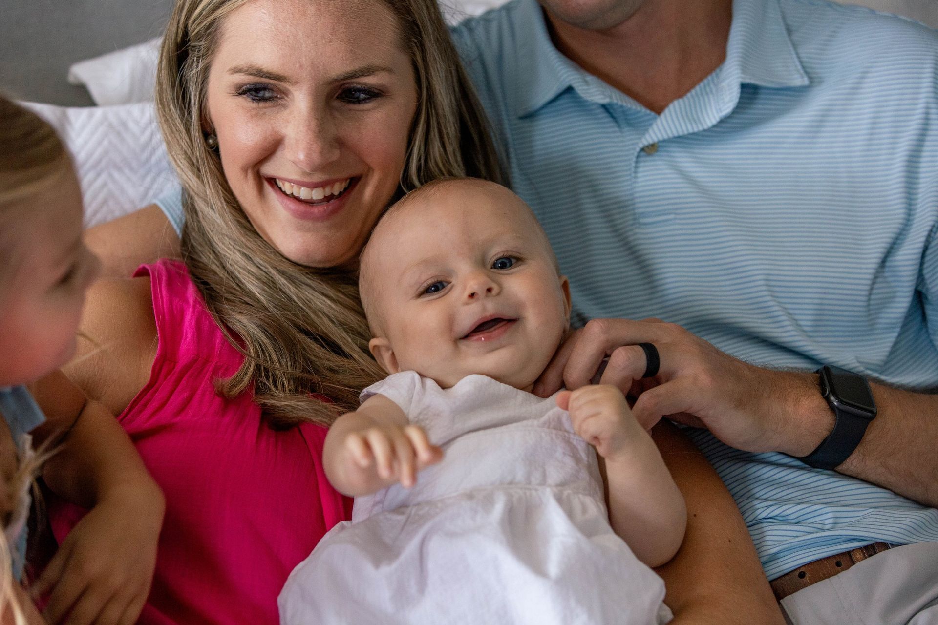 A family is sitting on a bed holding a baby.