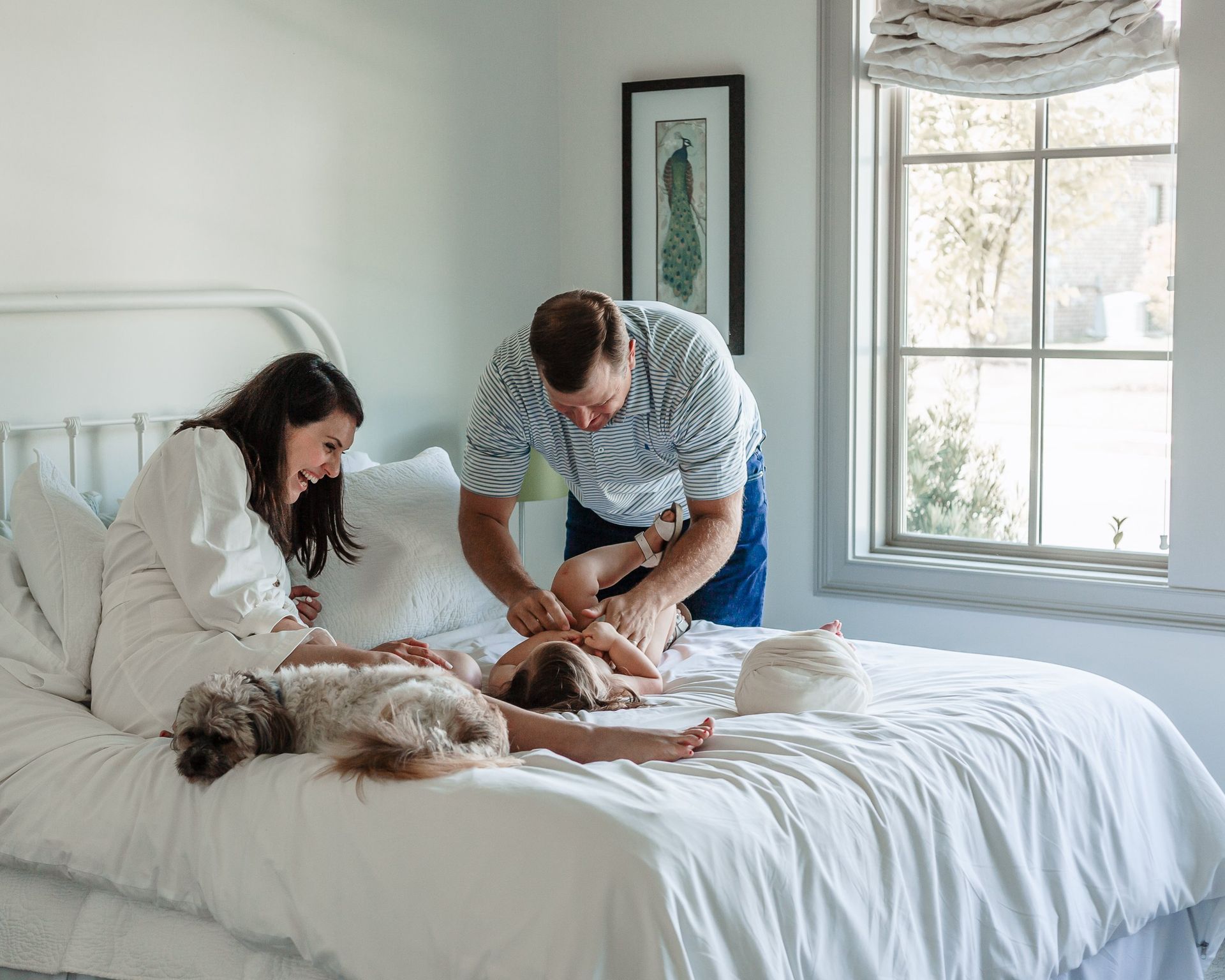 A family is playing with a baby on a bed.