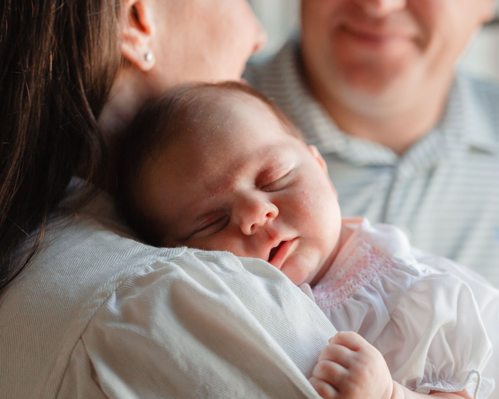 A woman is holding a baby in her arms while a man looks on.