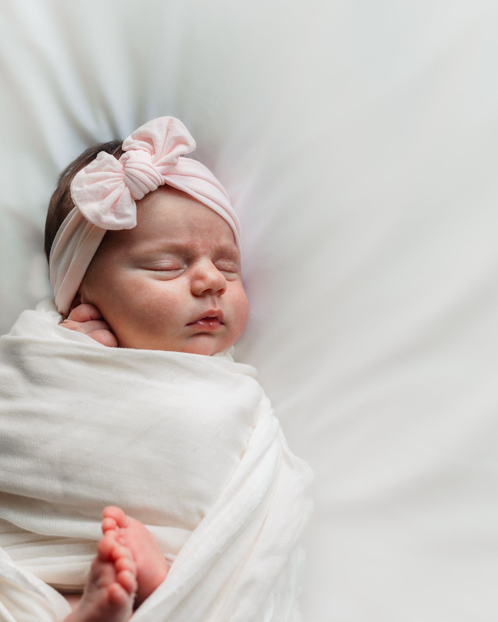 A newborn baby is wrapped in a white blanket and wearing a pink headband.
