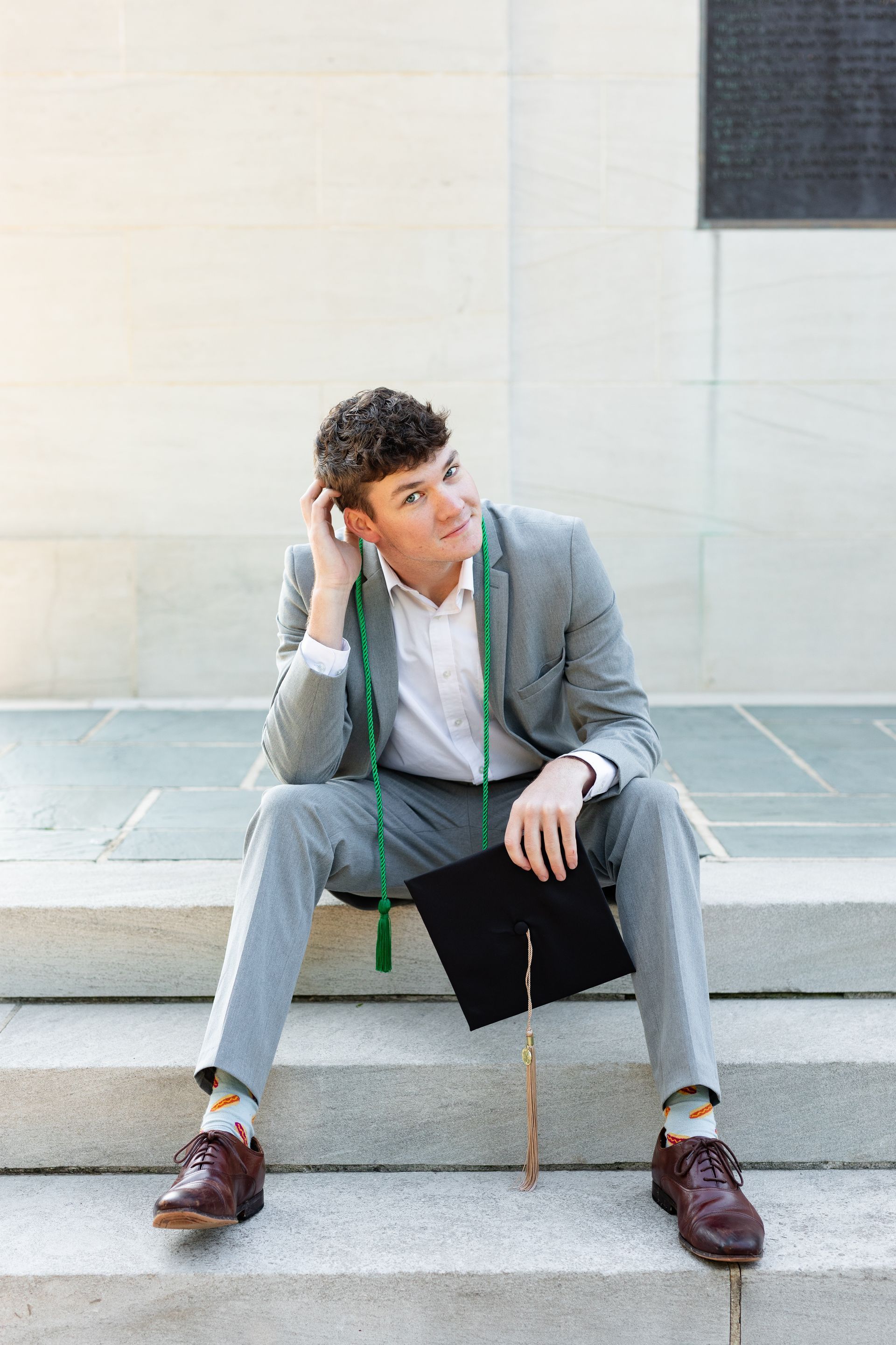 A man in a suit and graduation cap is sitting on the steps of a building.