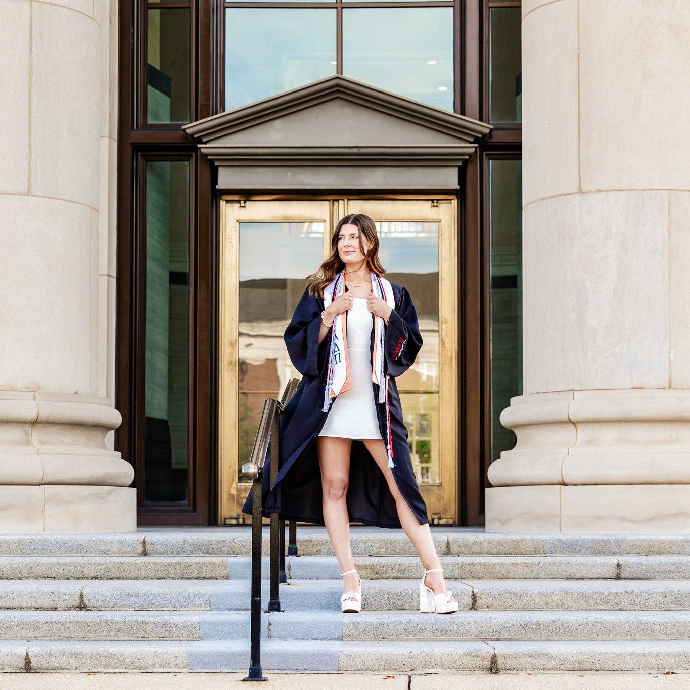 A woman in a graduation cap and gown is standing on the steps of a building.