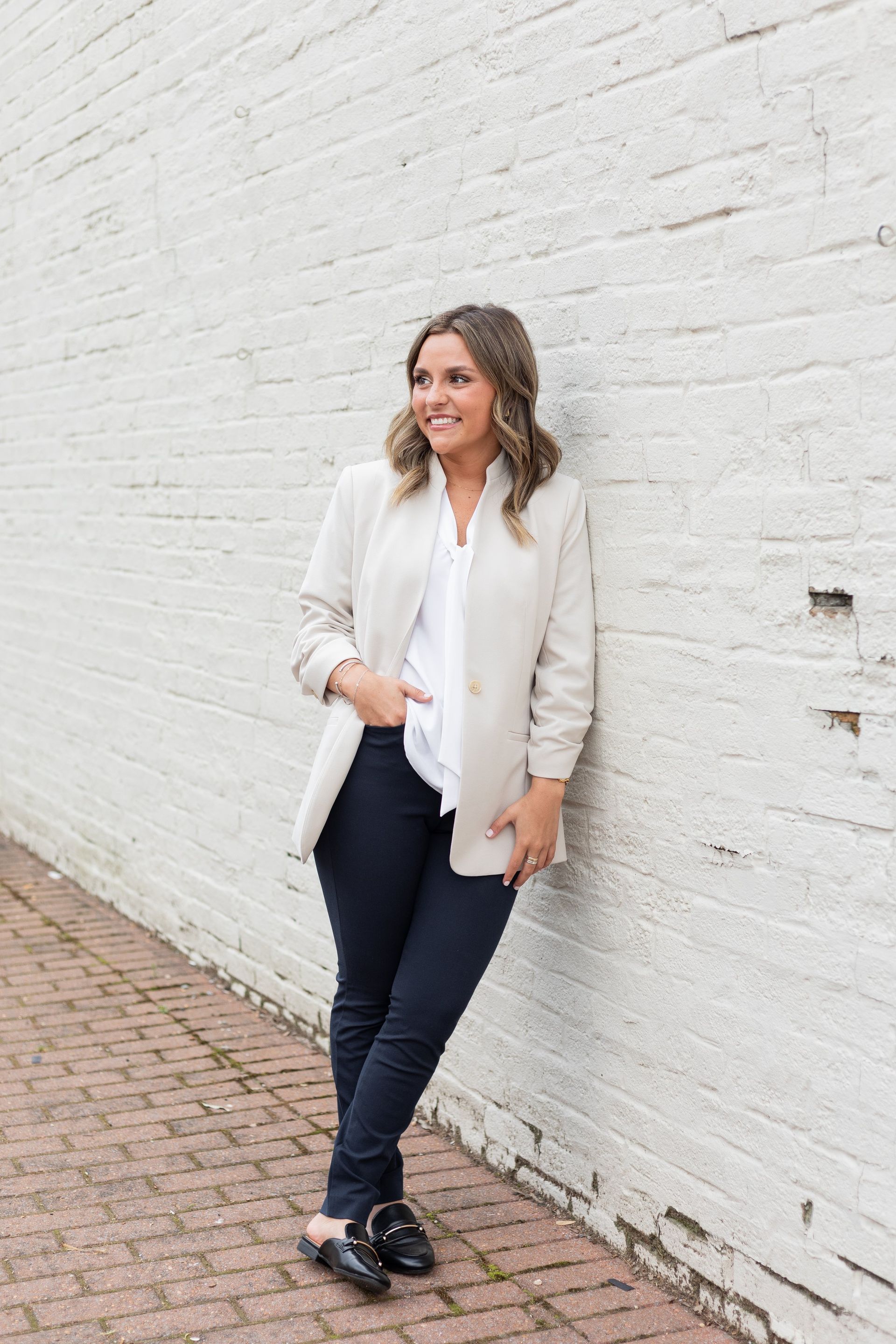 A woman is leaning against a white brick wall on a sidewalk.