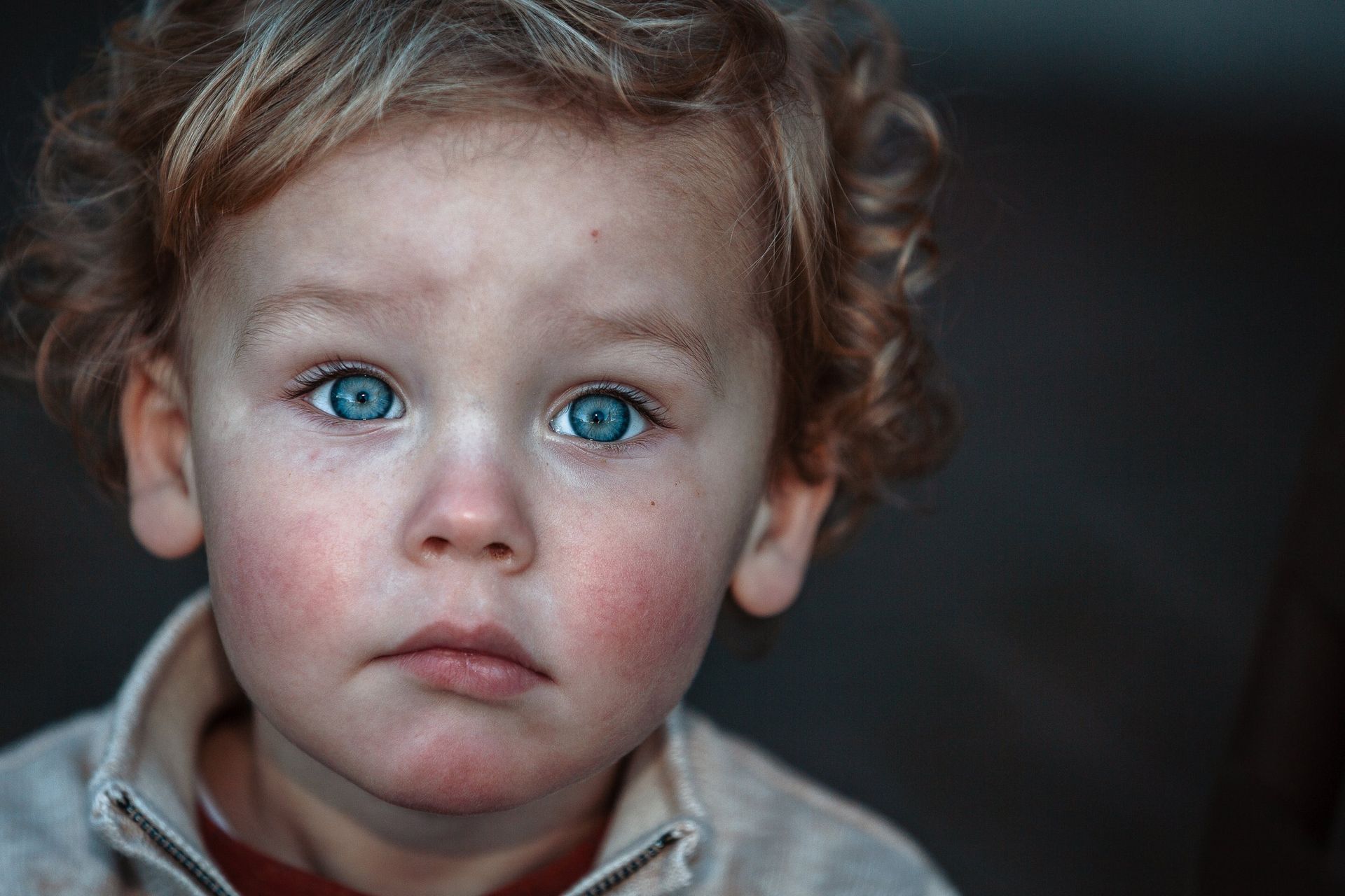A young boy with blue eyes is looking at the camera with a sad look on his face.