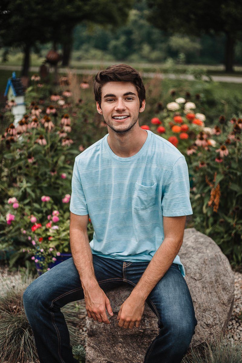 A young man is sitting on a rock in front of a flower garden.