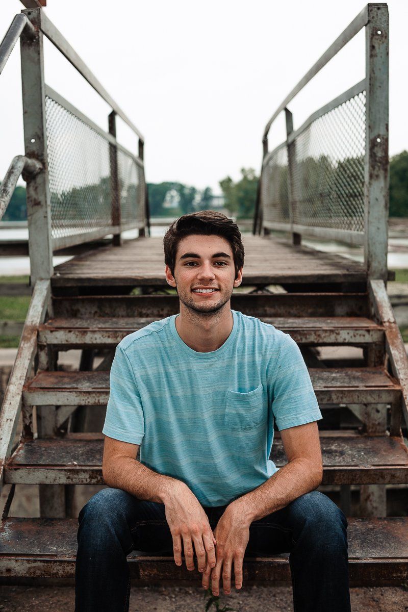 A young man is sitting on a set of stairs in front of a bridge.