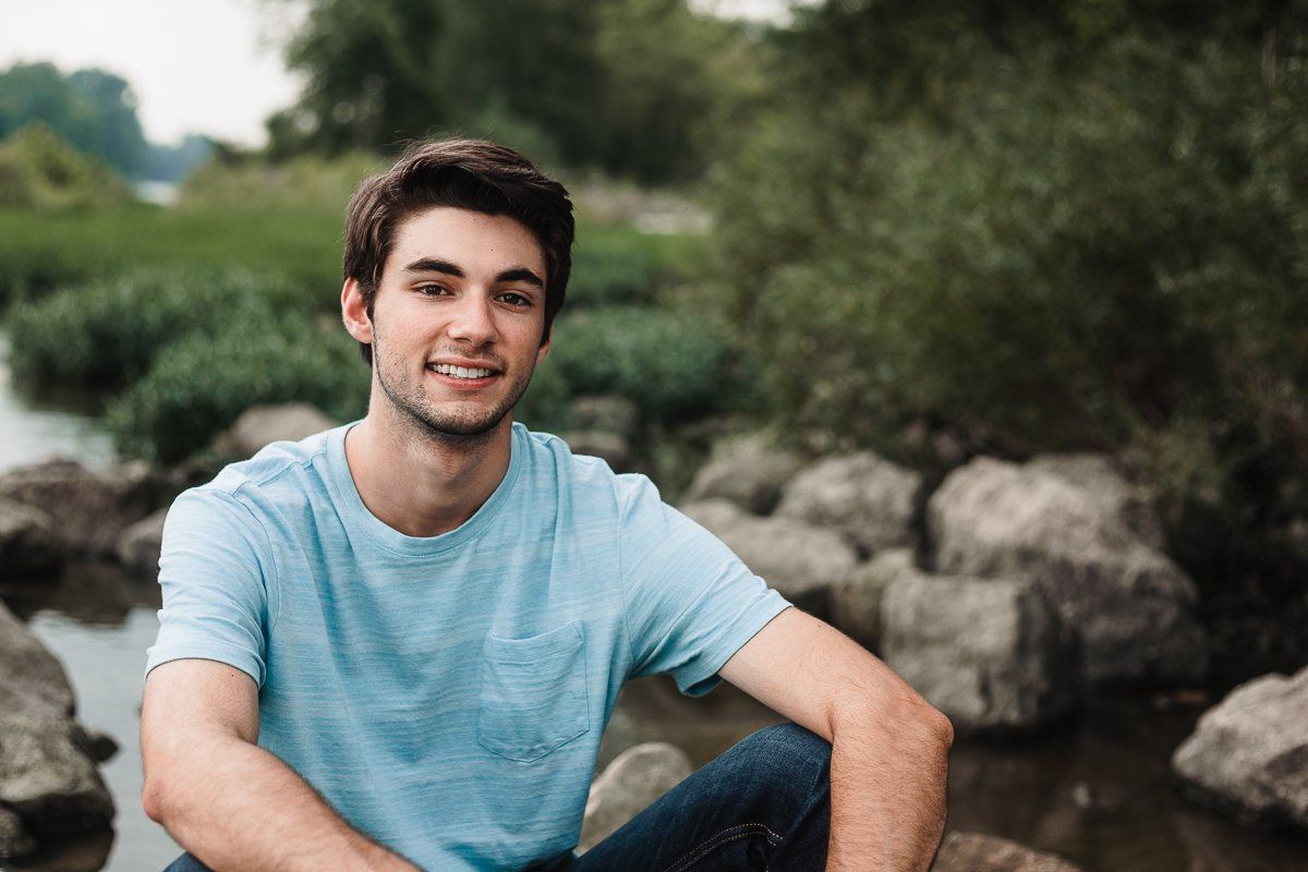 A young man is sitting on a rock near a river.