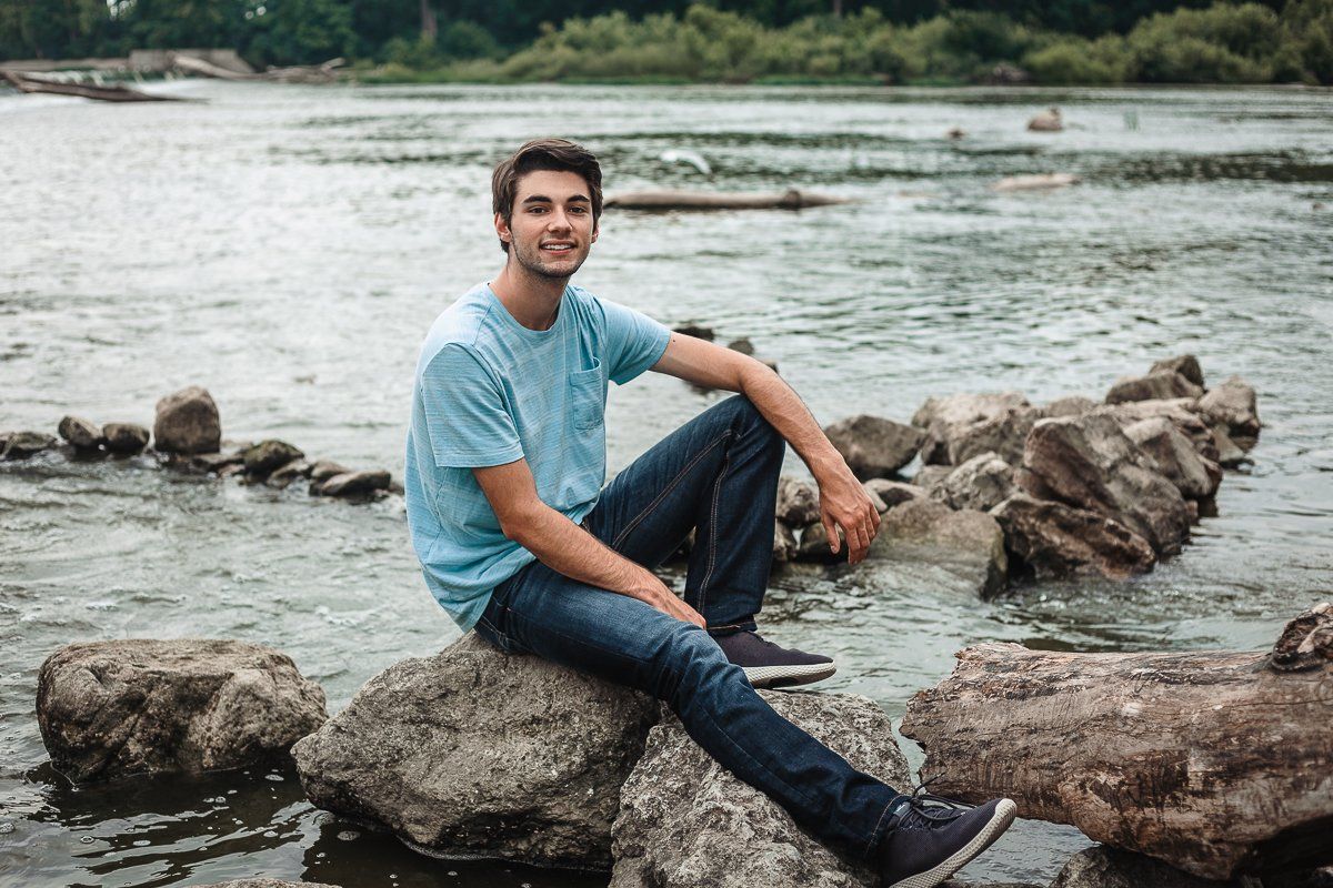 A young man is sitting on a rock by the water.