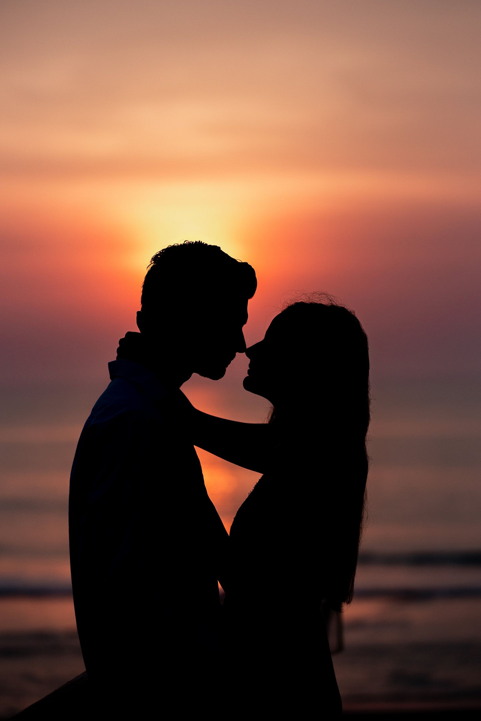 A man and a woman are kissing on the beach at sunset.