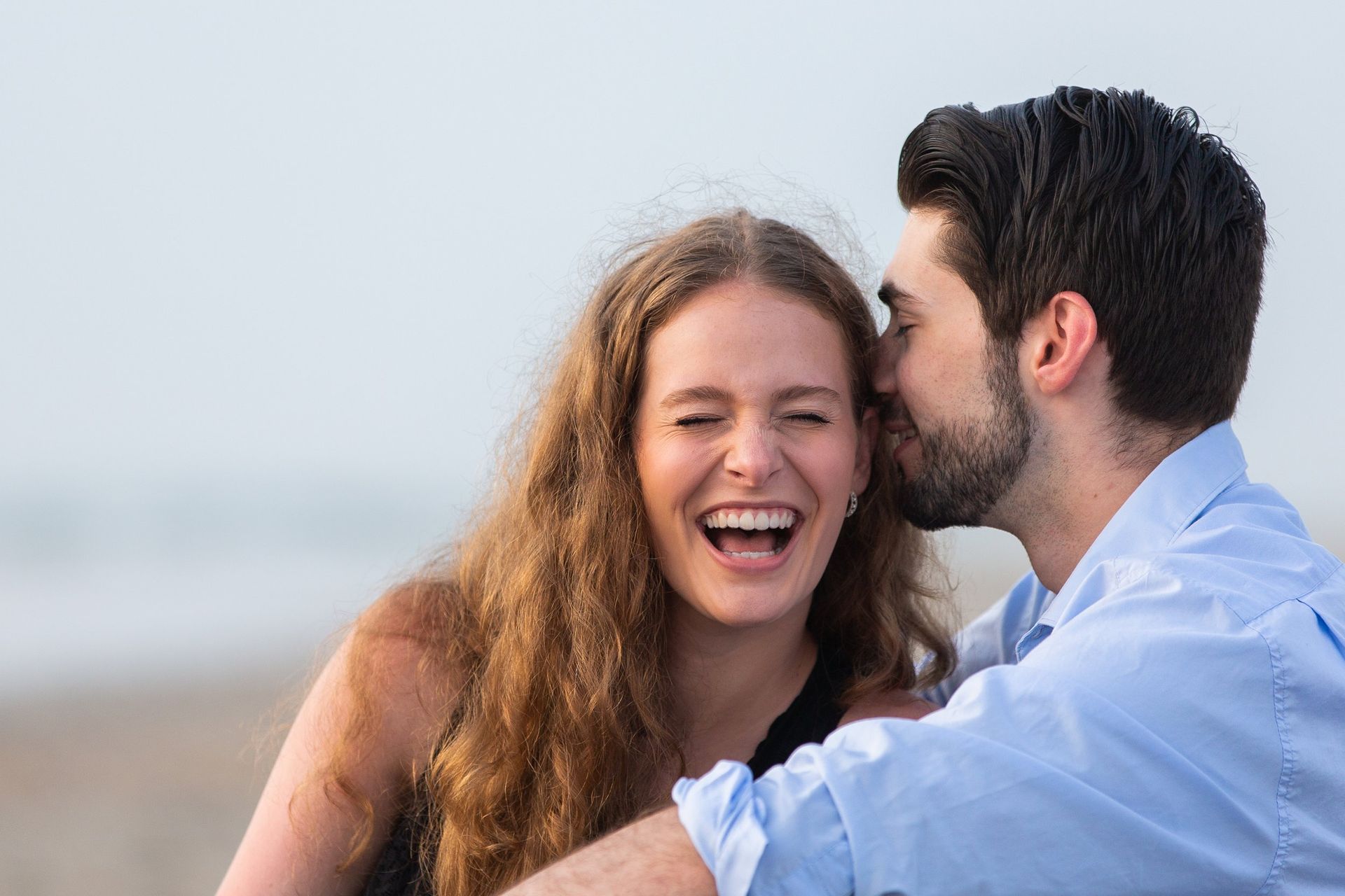 A man is kissing a woman on the cheek on the beach.