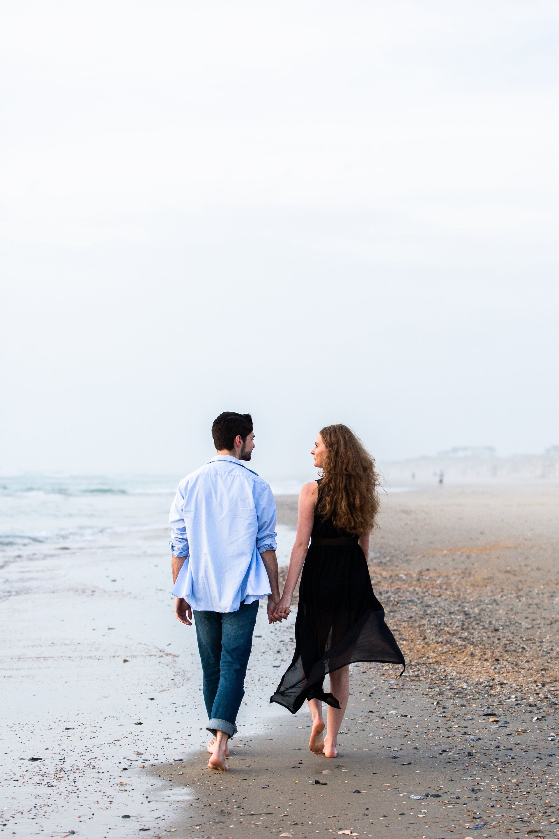 A man and a woman are walking on the beach holding hands.