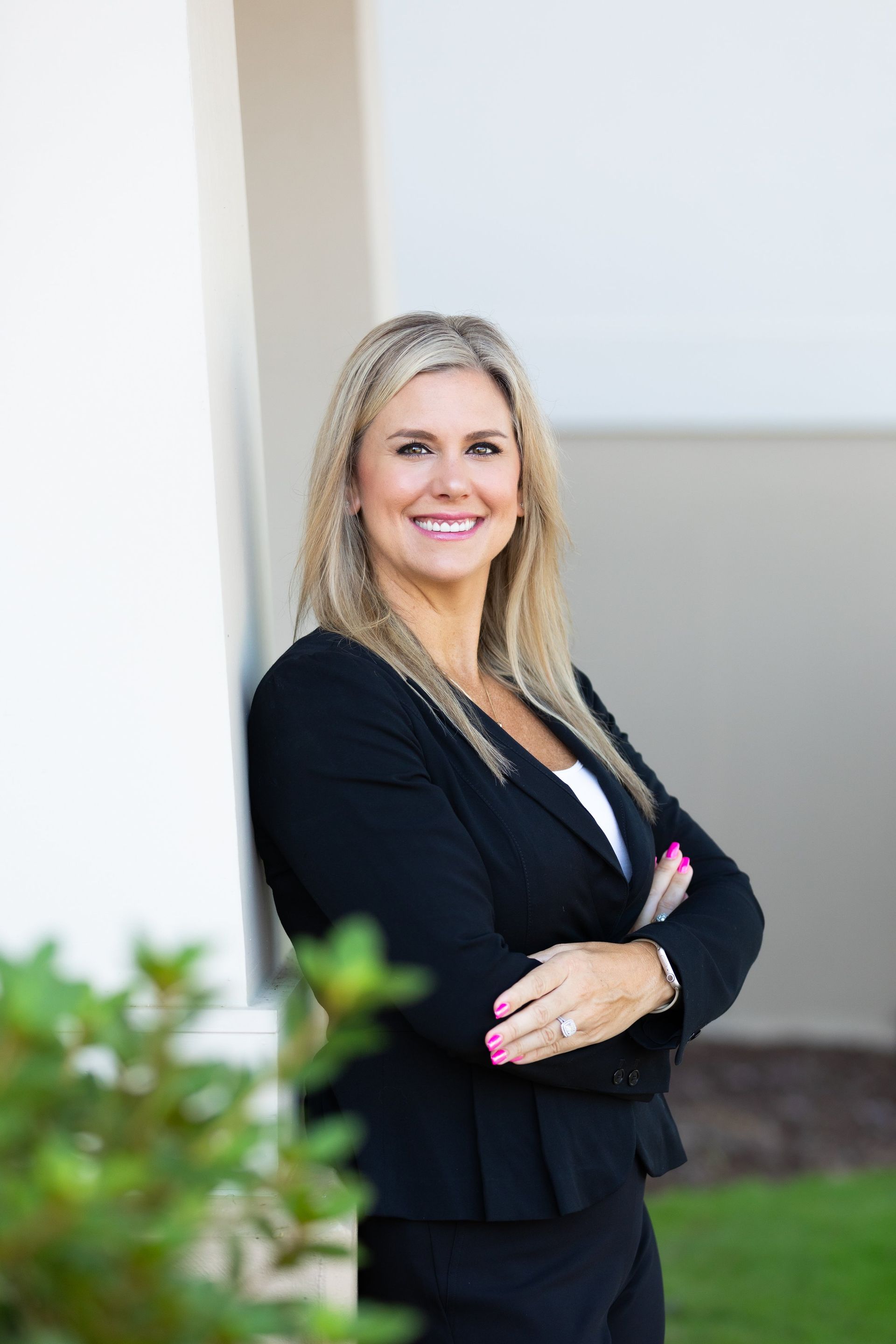 A woman in a black suit is standing in front of a building with her arms crossed.