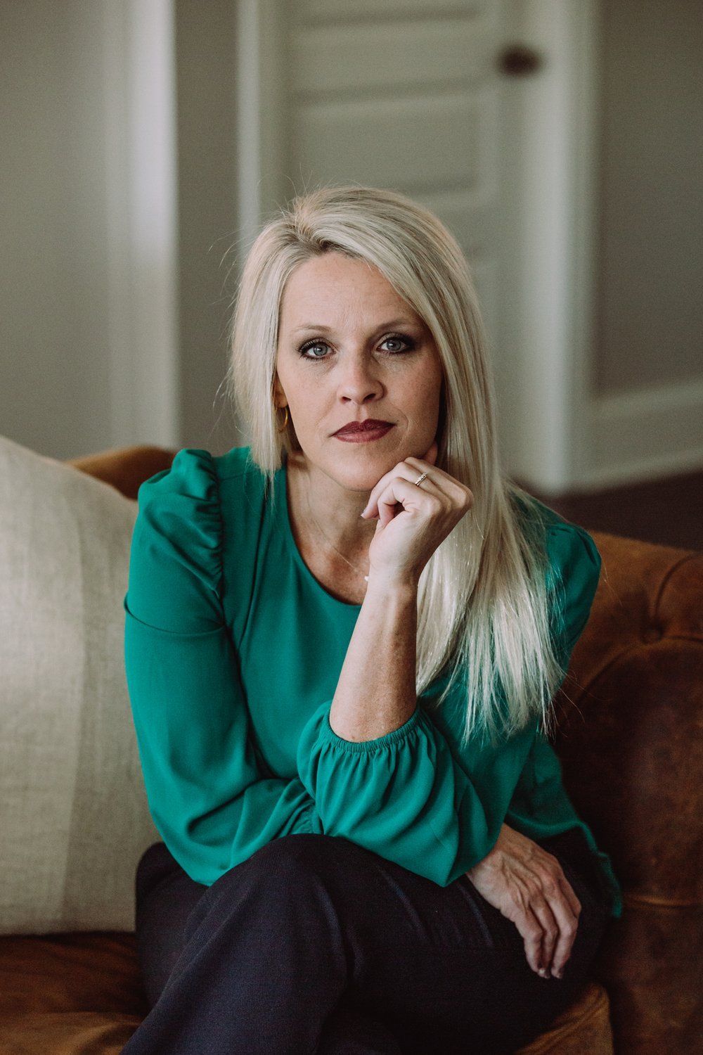 A woman in a green shirt is sitting on a couch with her hand on her chin.