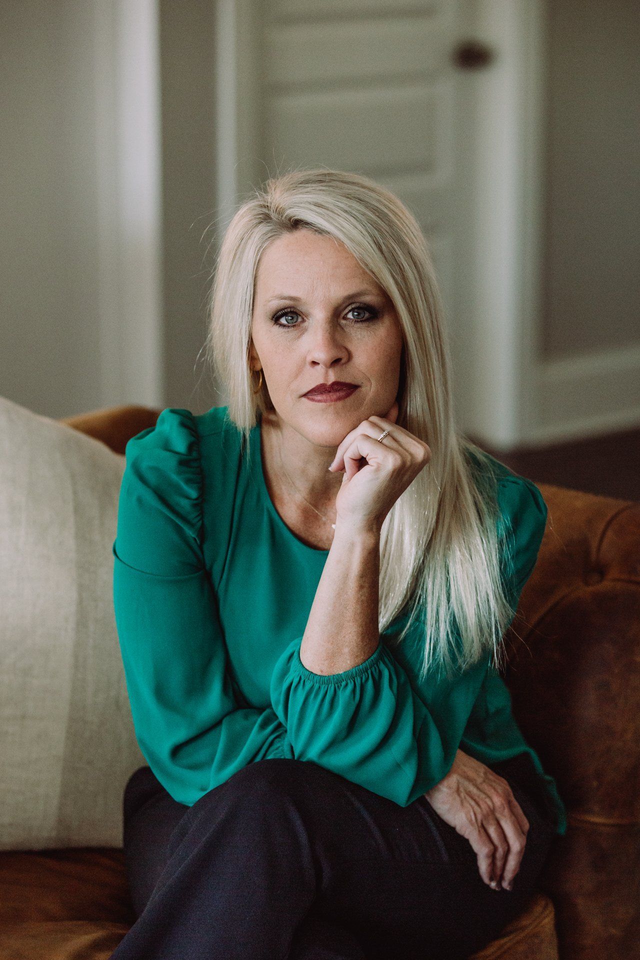 A woman in a green shirt is sitting on a couch with her hand on her chin.