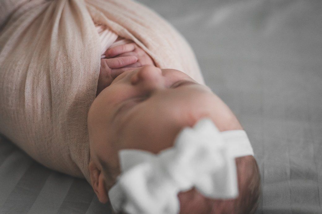 A newborn baby wrapped in a pink blanket with a white bow on her head.