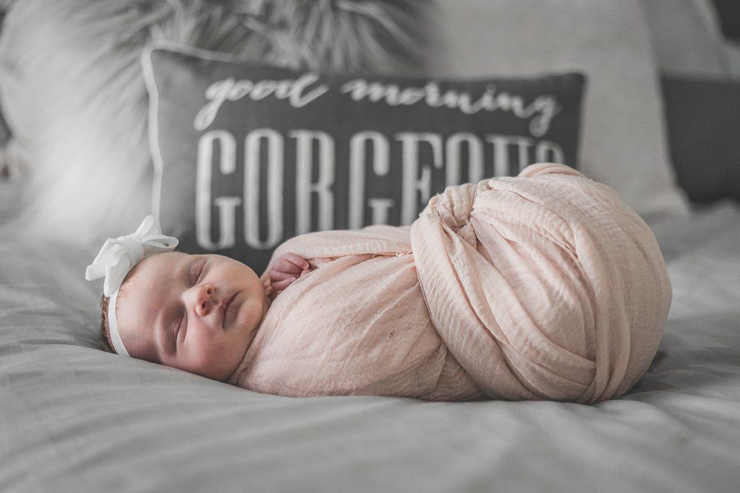 A newborn baby is sleeping on a bed next to a pillow that says `` good morning gorgeous ''.