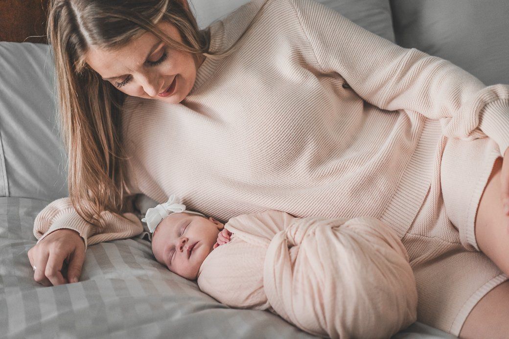 A woman is laying on a bed with a newborn baby wrapped in a blanket.