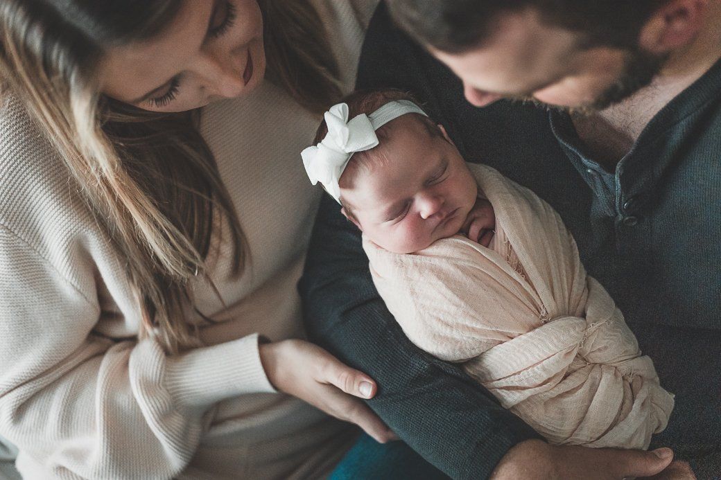 A man and woman are holding a newborn baby wrapped in a blanket.