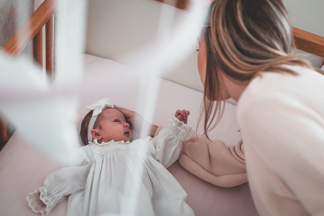 A woman is playing with a baby in a crib.
