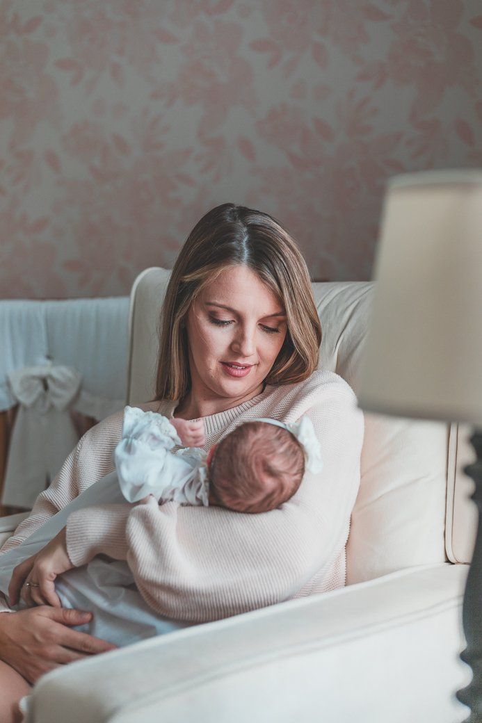 A woman is holding a newborn baby in her arms while sitting in a chair.