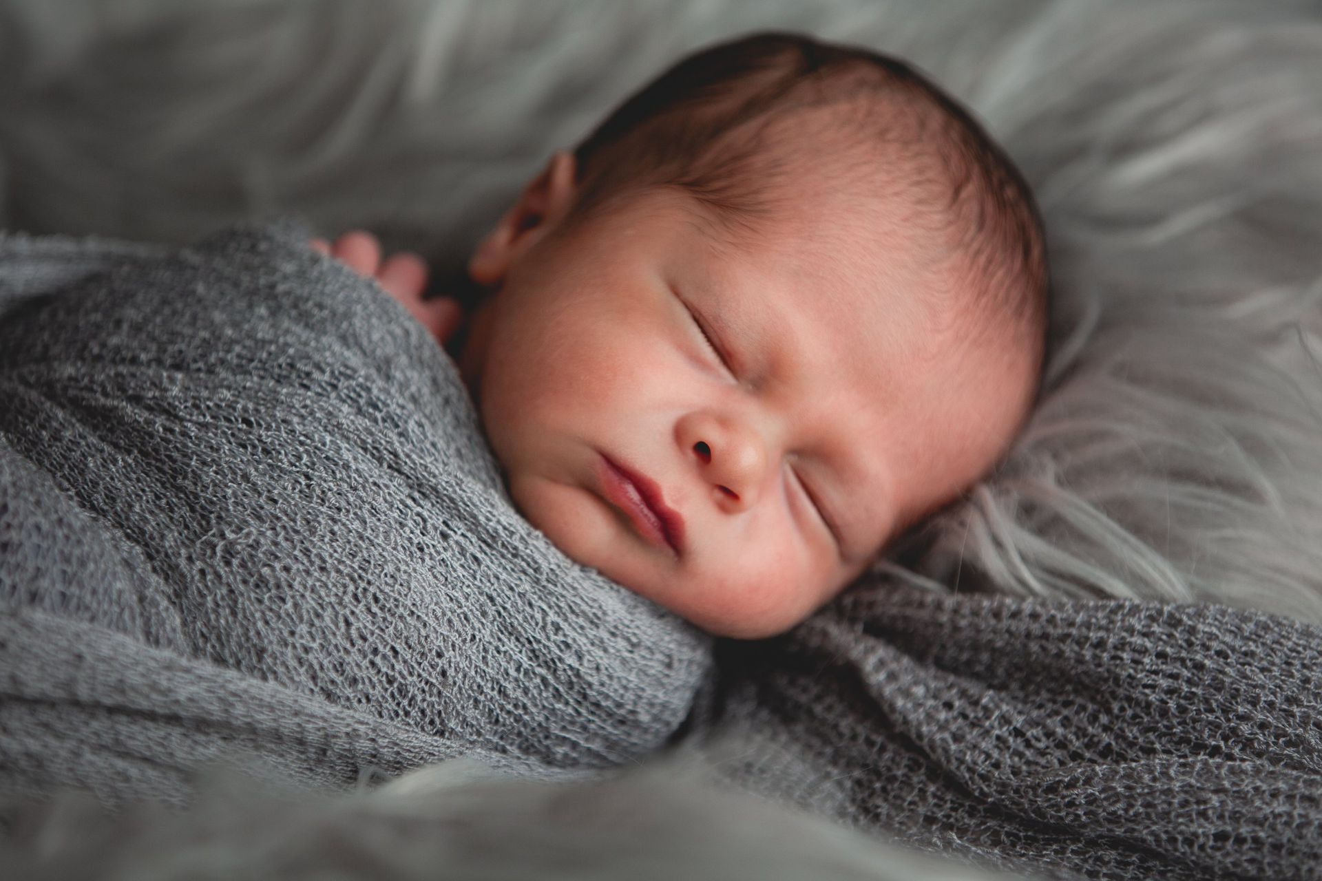 A newborn baby wrapped in a grey blanket is sleeping on a bed.