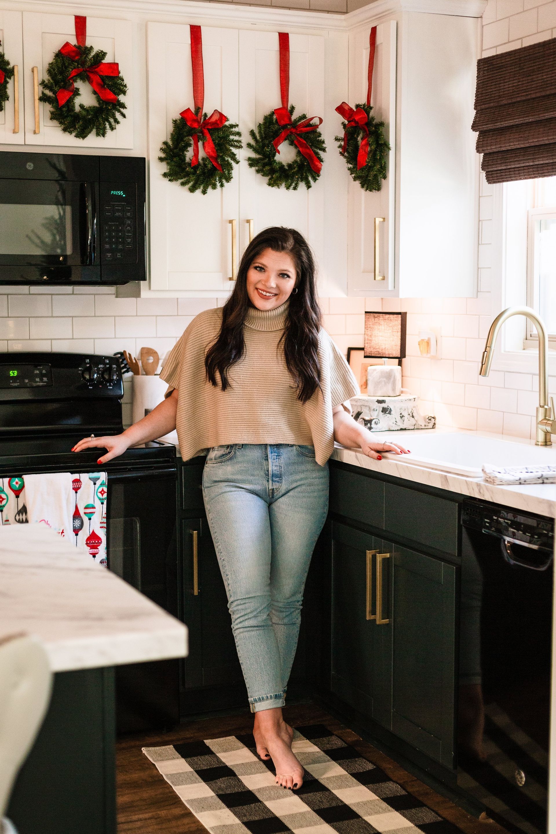 A woman is standing in a kitchen with christmas wreaths on the wall.
