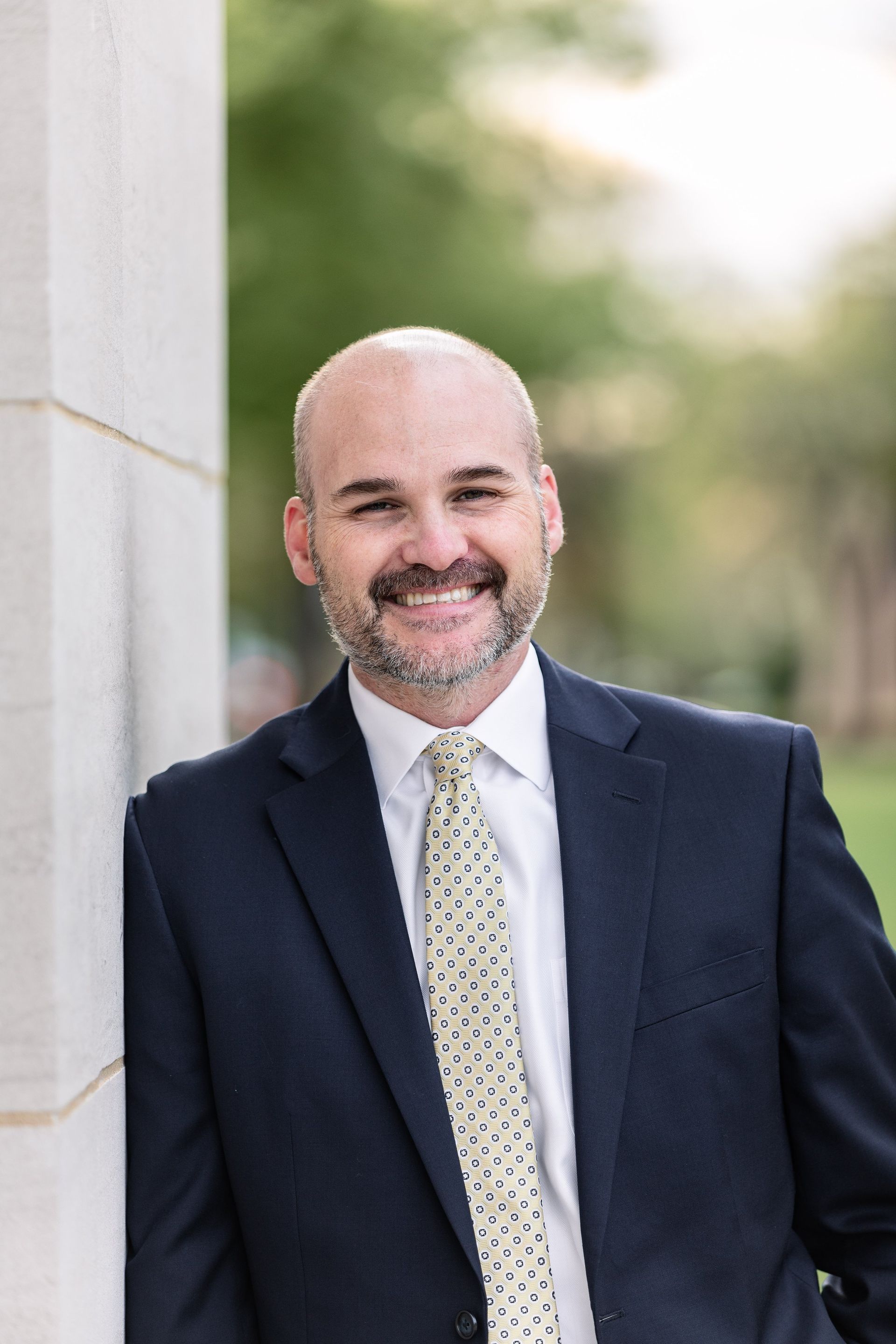 A man in a suit and tie is leaning against a wall and smiling.