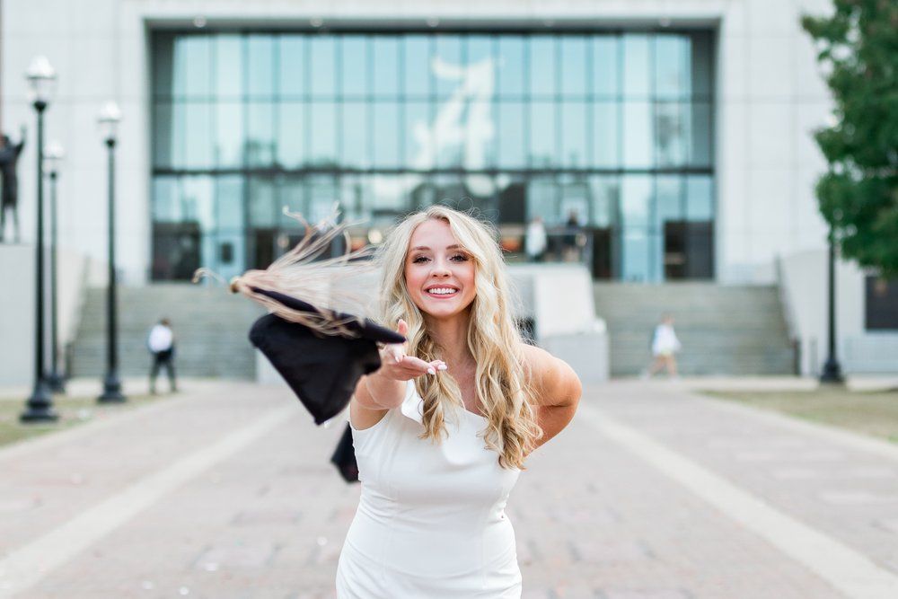 A woman in a white dress is throwing her graduation cap in the air.