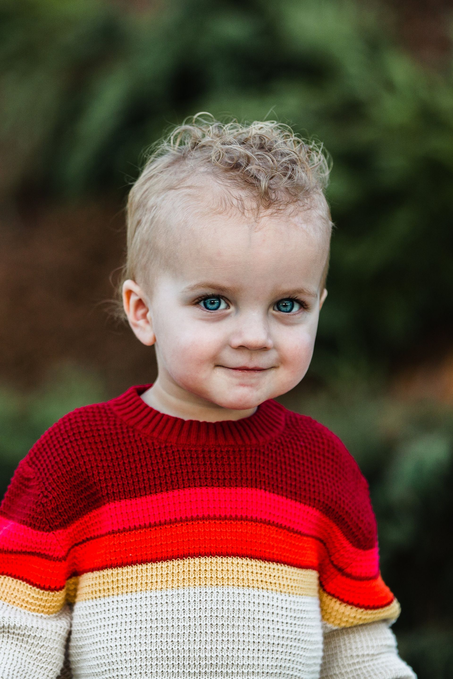 A young boy with curly hair is wearing a striped sweater.