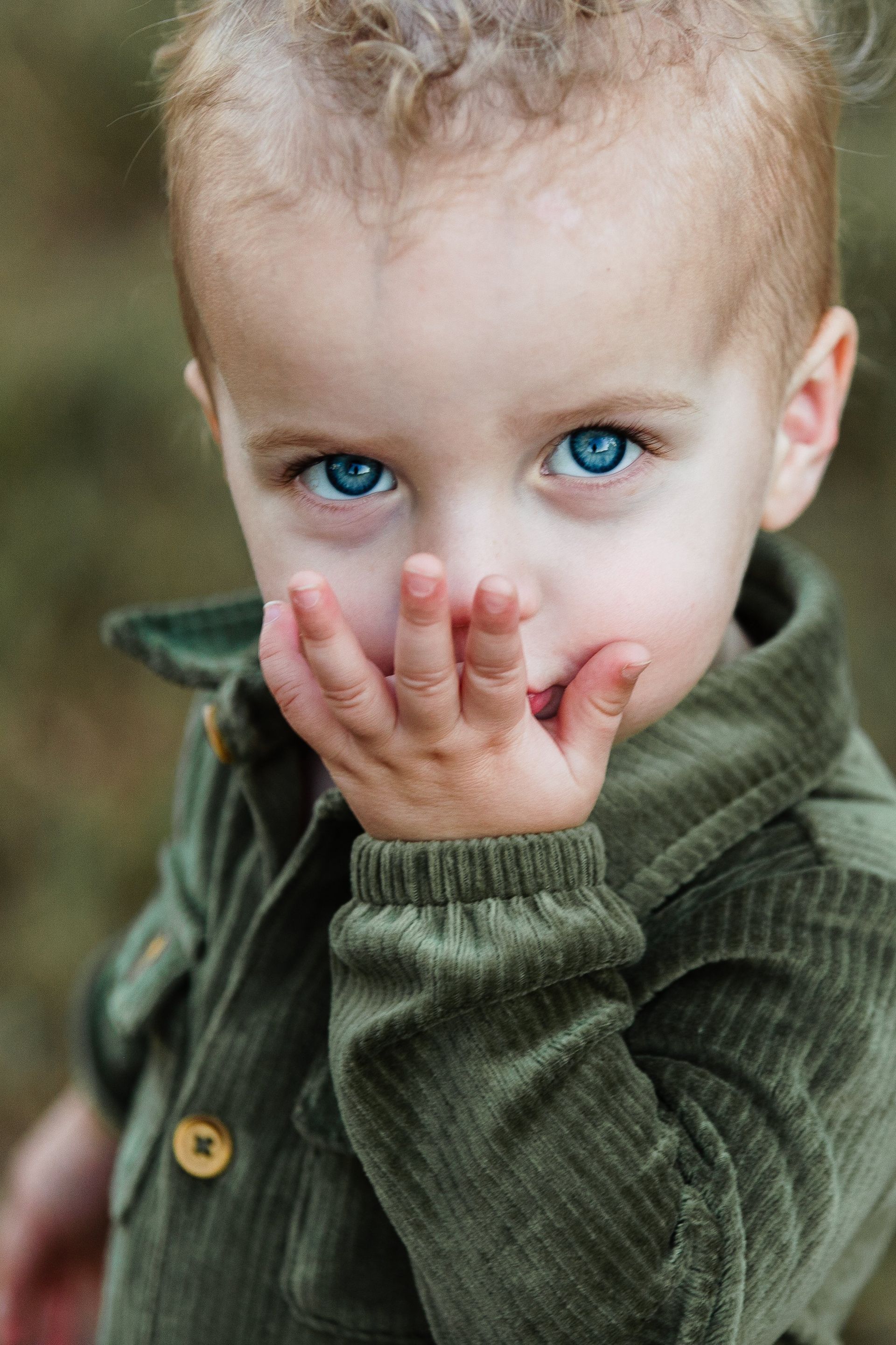 A little boy with blue eyes is covering his mouth with his hand.