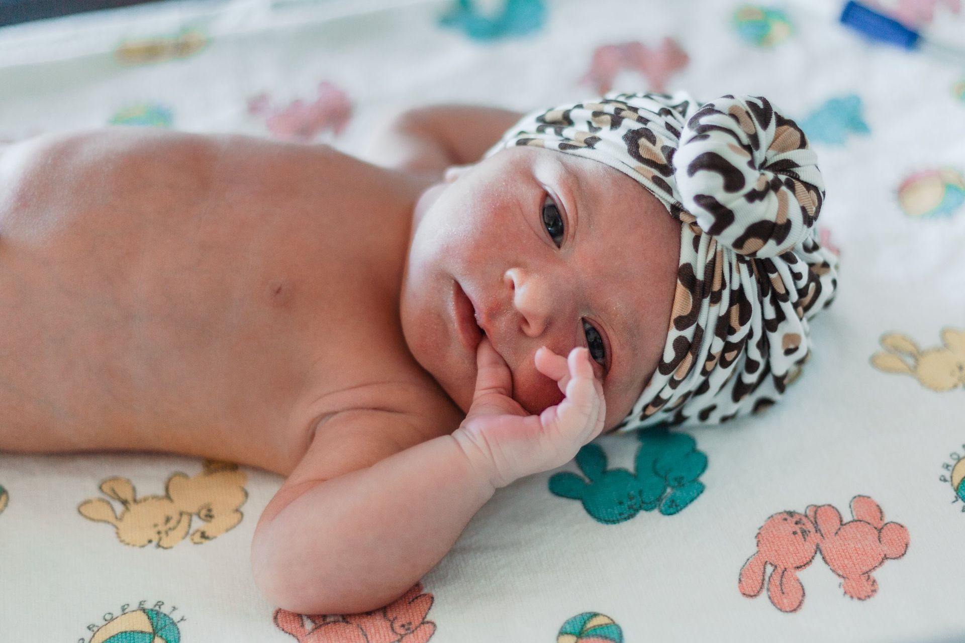 A newborn baby wearing a leopard print hat is laying on a blanket.