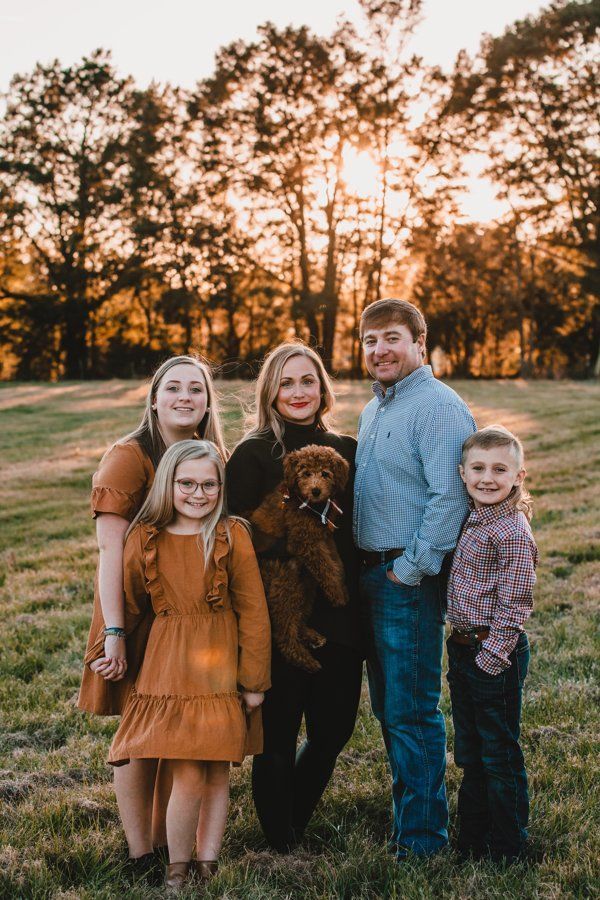 A family is posing for a picture in a field with a dog.