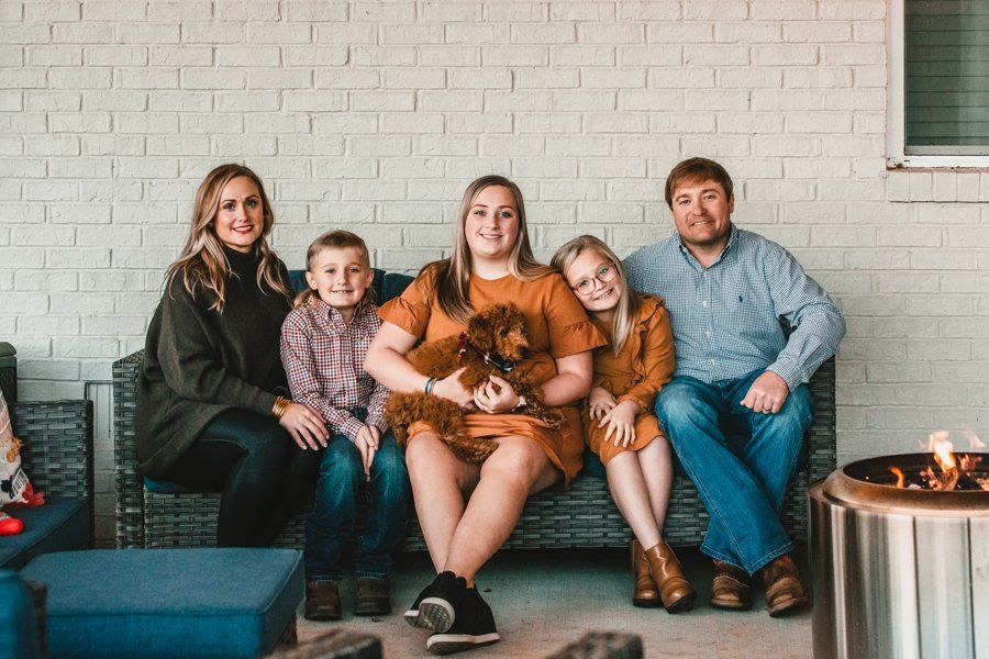 A family is sitting on a couch on a porch with a dog.
