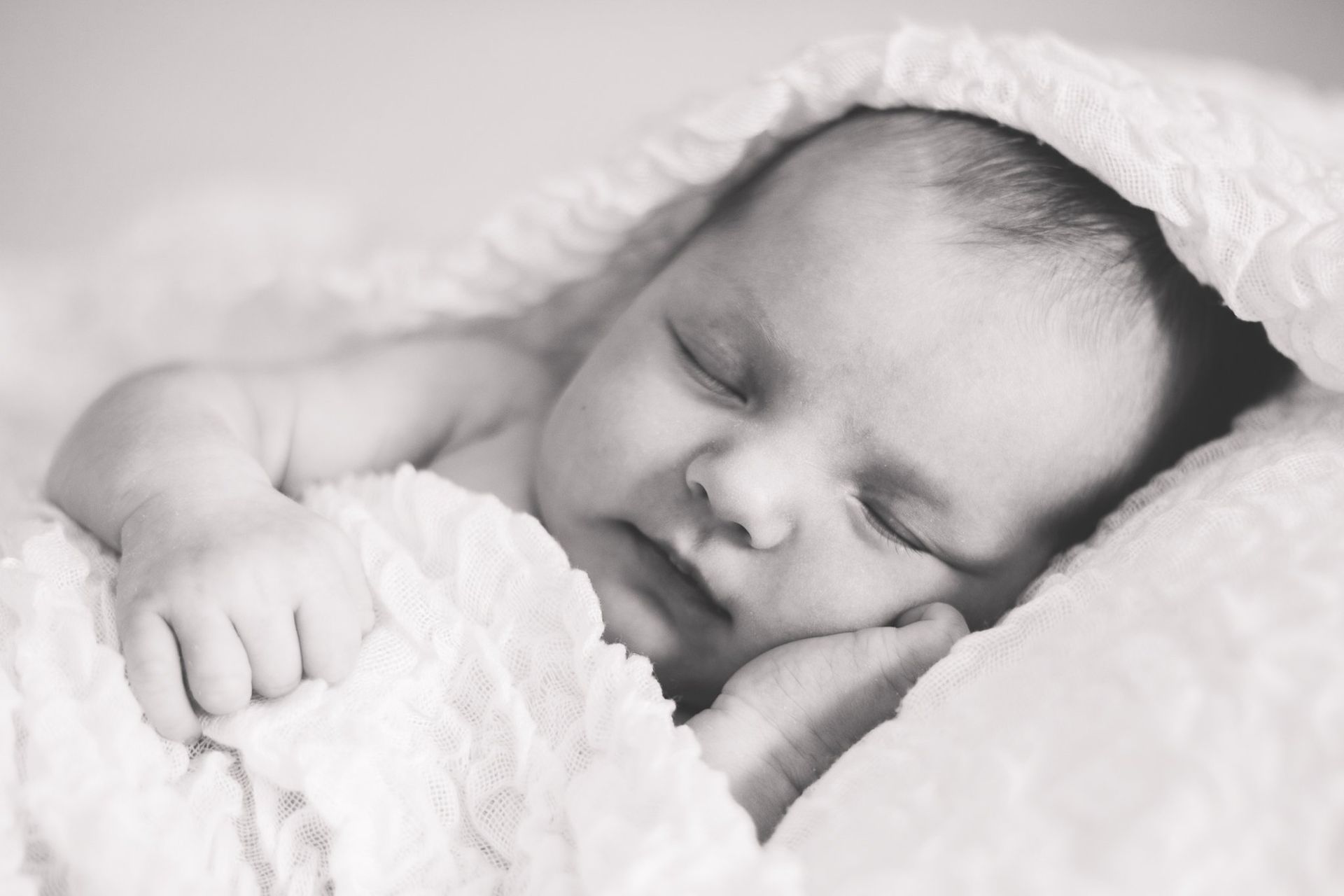 A black and white photo of a newborn baby wrapped in a white blanket.