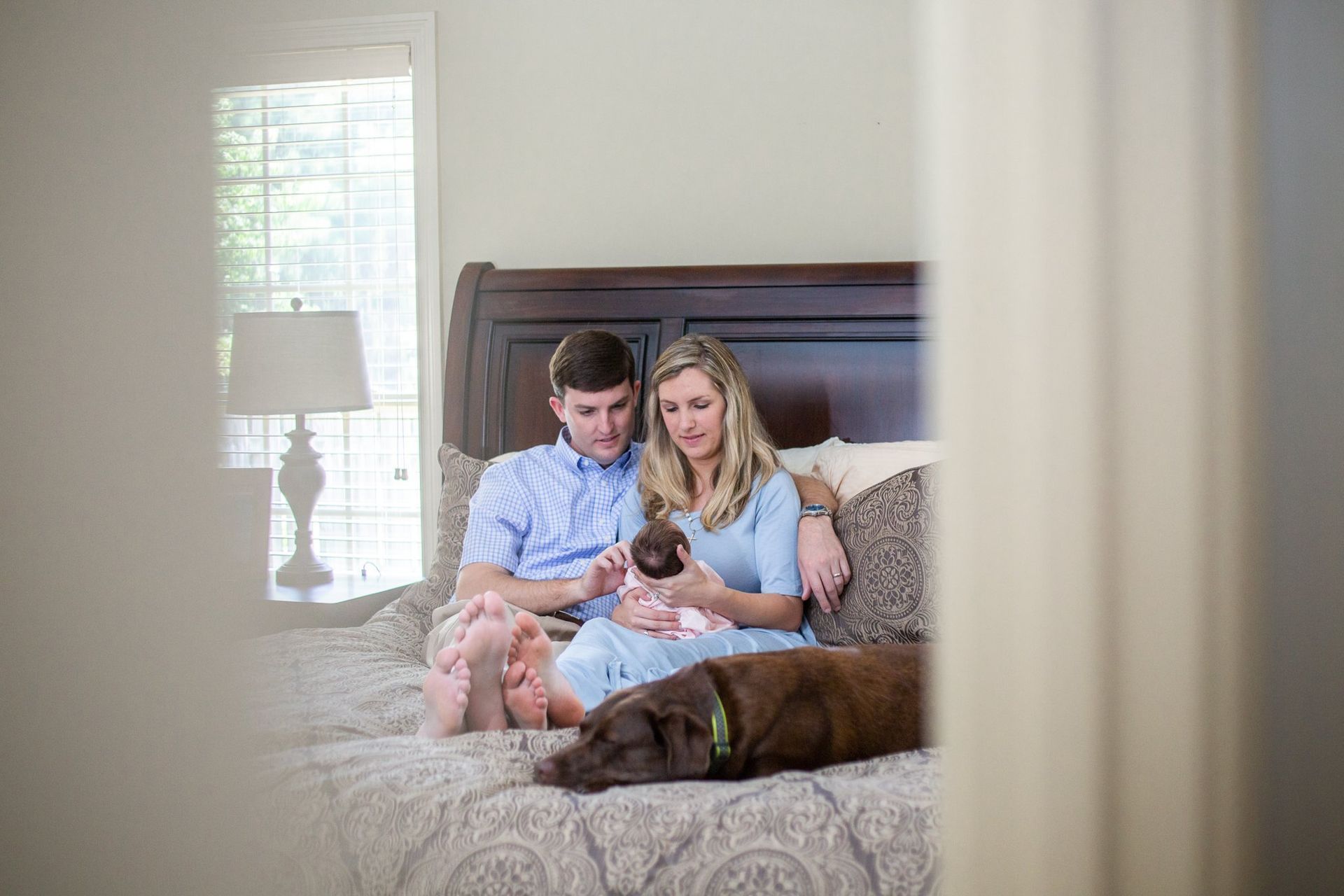 A man and woman are sitting on a bed with a newborn baby and a dog.