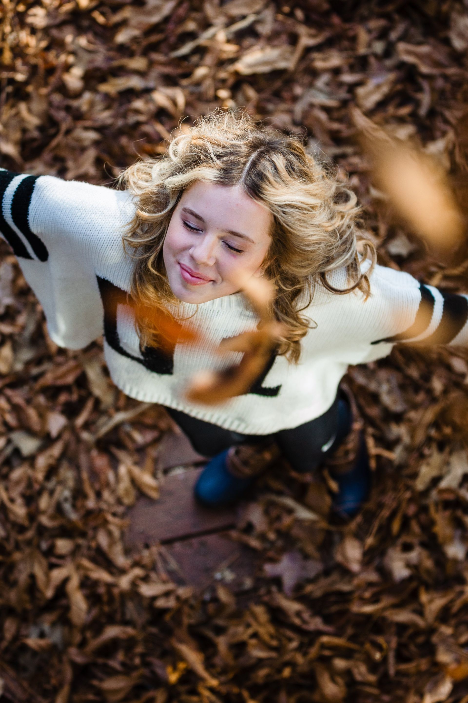 A woman in a white sweater is throwing leaves in the air.