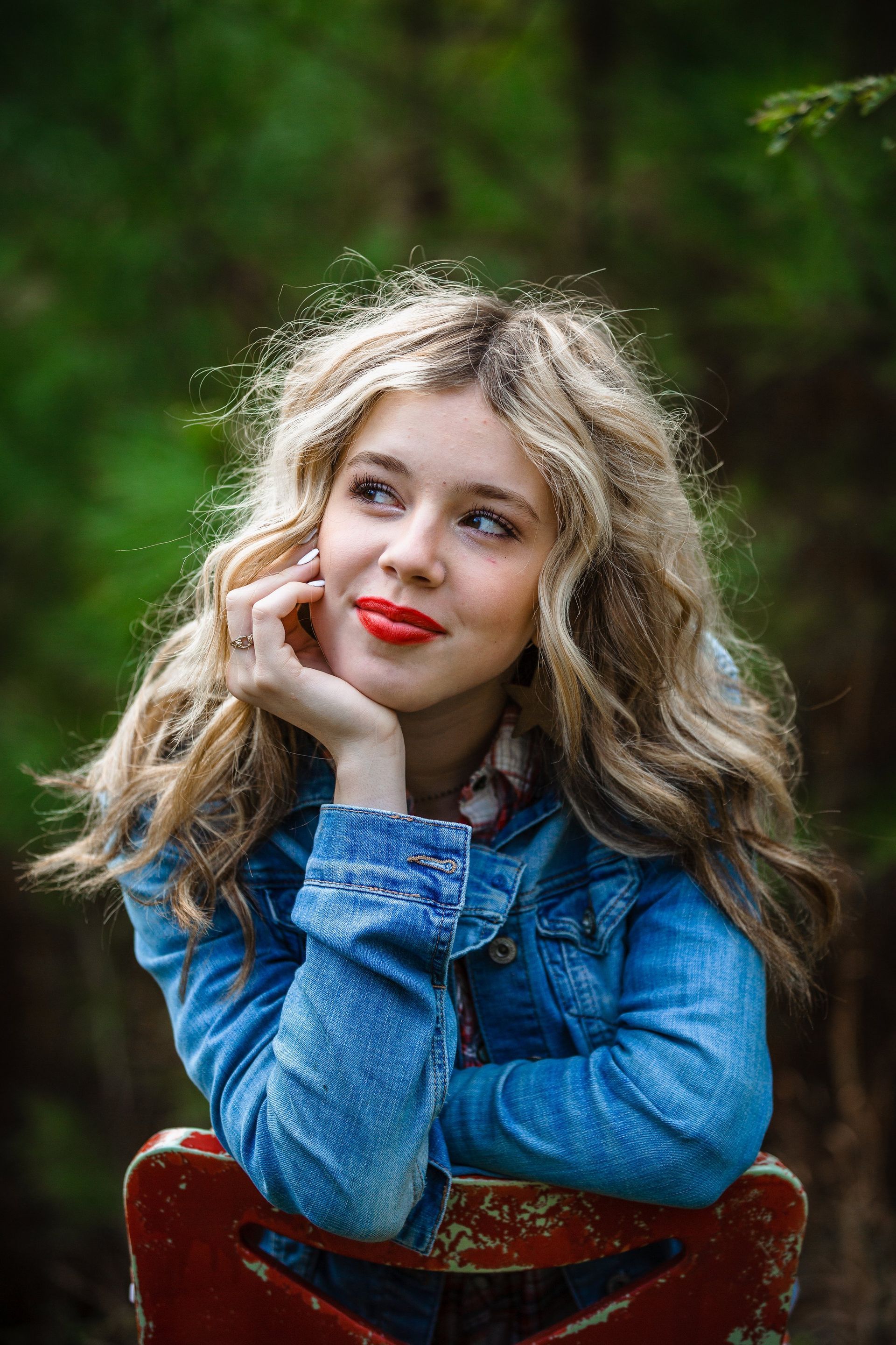 A young woman in a denim jacket and red lipstick is sitting on a red chair.