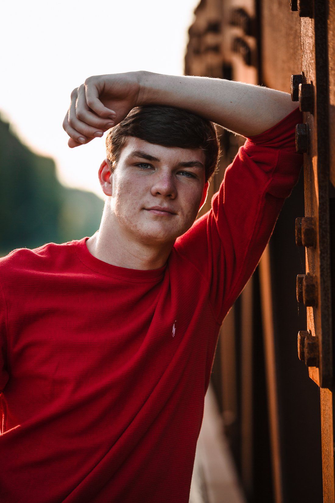 A young man in a red shirt is leaning against a wall.