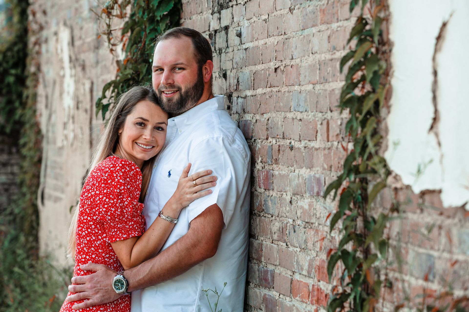 A man and a woman are hugging each other in front of a brick wall.